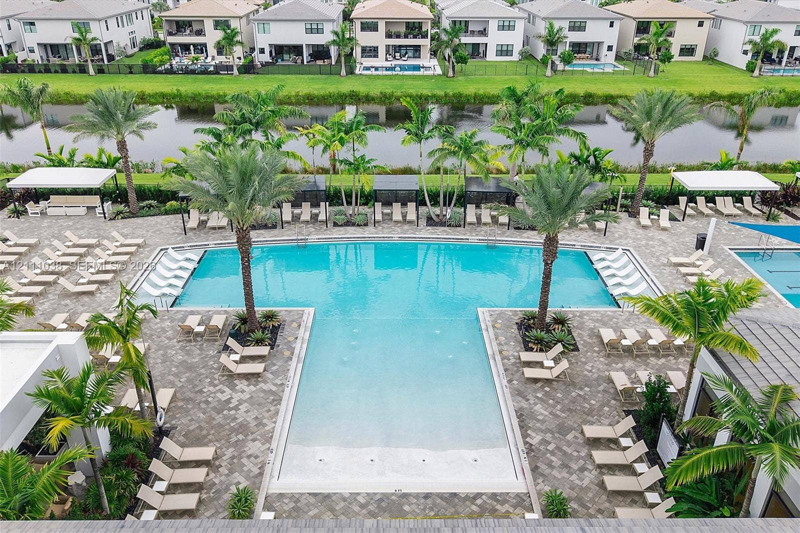 Community pool featuring a shallow sun shelf, paver surround, mature palm trees, and covered cabanas