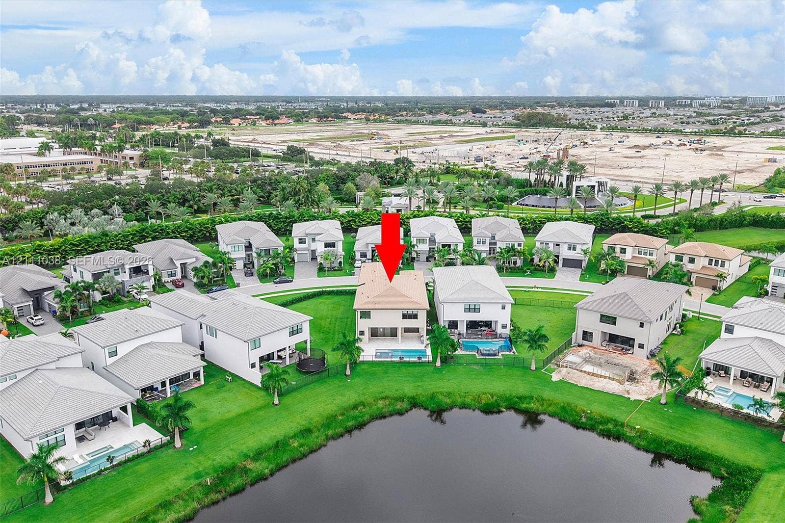 Two-story residence featuring a tile roof, an in-ground swimming pool, and water frontage on a decorative pond, situated on a manicured lot with mature palm trees