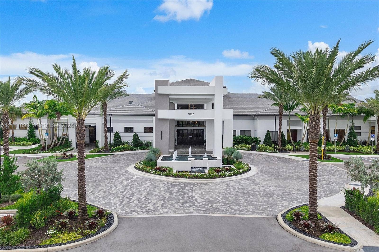 Contemporary exterior featuring a structured geometric entryway, a circular paver driveway, a central water feature, and mature palm landscaping