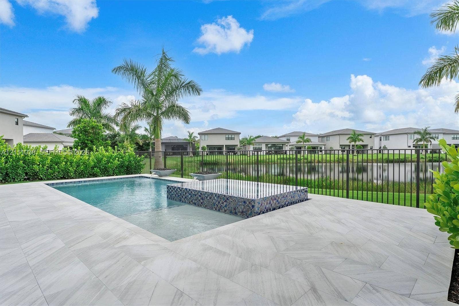 In-ground pool featuring a raised, tiled spillover spa, large-format porcelain paver decking, and a metal perimeter fence
