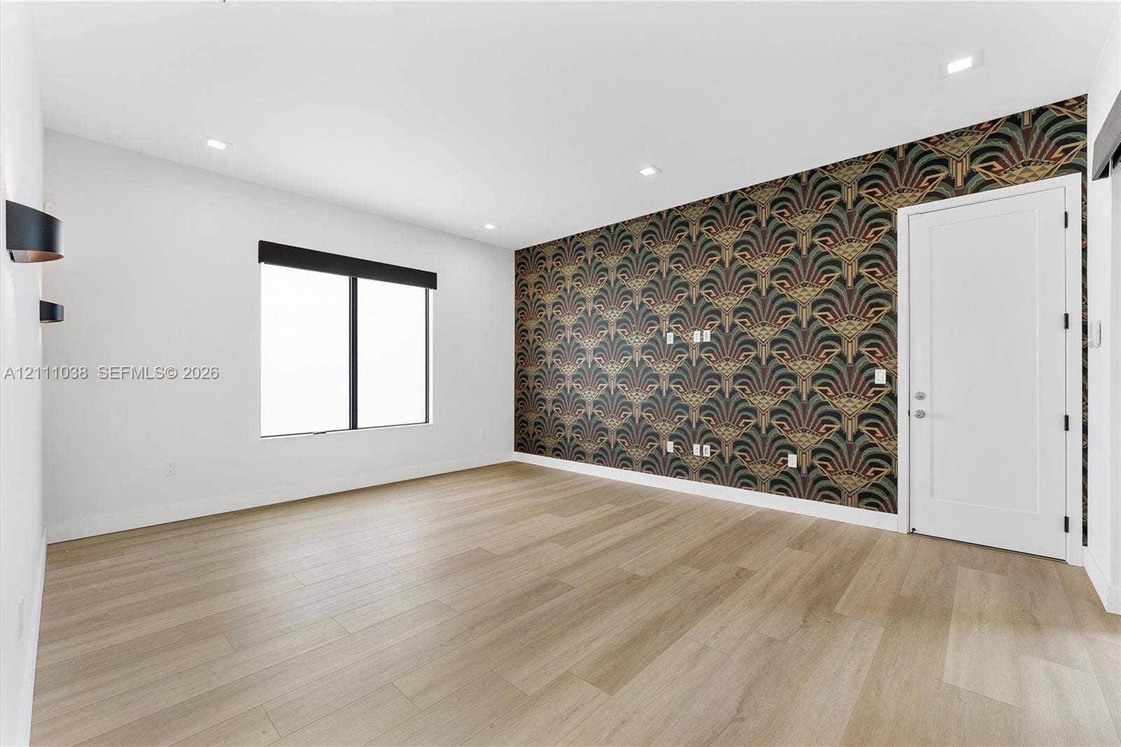 Light-filled room featuring wood-finish flooring, a decorative patterned accent wall, recessed lighting, and matte black wall-mounted light fixtures