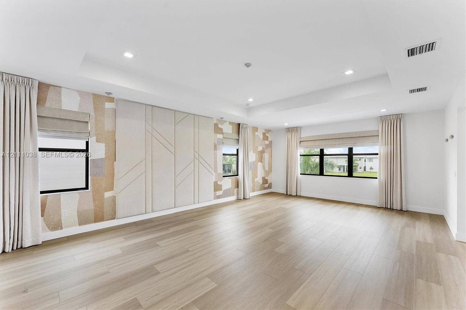 Tray ceiling featuring recessed lighting, light wood-finish flooring, and wall panels with textured geometric detailing