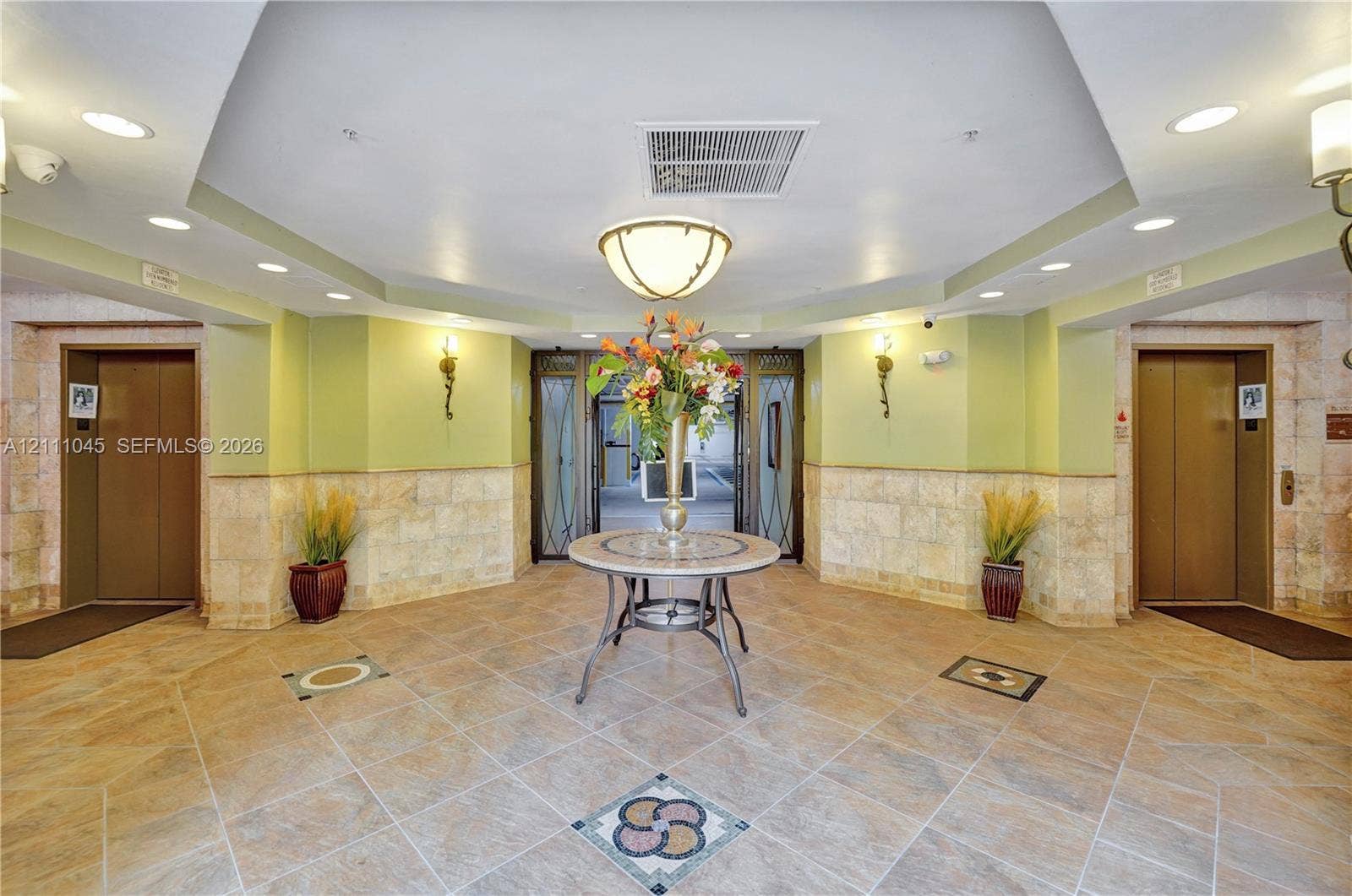 2901 NW 126th Avenue, #2-225, Sunrise, FL 33323 Lobby featuring octagonal tray ceiling with recessed lighting, stone tile flooring with decorative inlay, dual elevators with metallic finish doors, and lower-wall stone masonry cladding