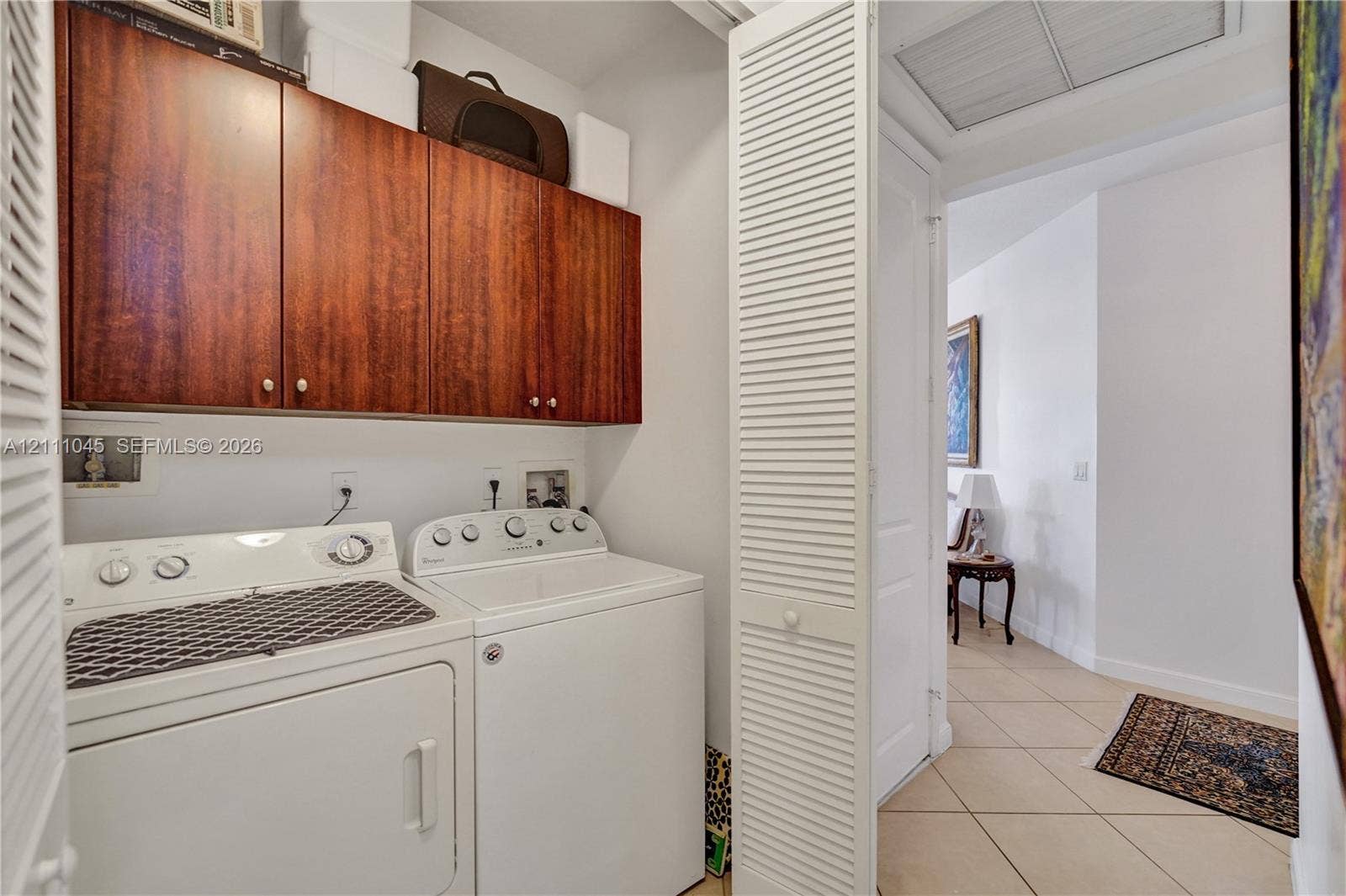 2901 NW 126th Avenue, #2-225, Sunrise, FL 33323 Laundry area featuring wood-finish wall-mounted cabinetry, louvered bi-fold closet doors, and ceramic tile flooring