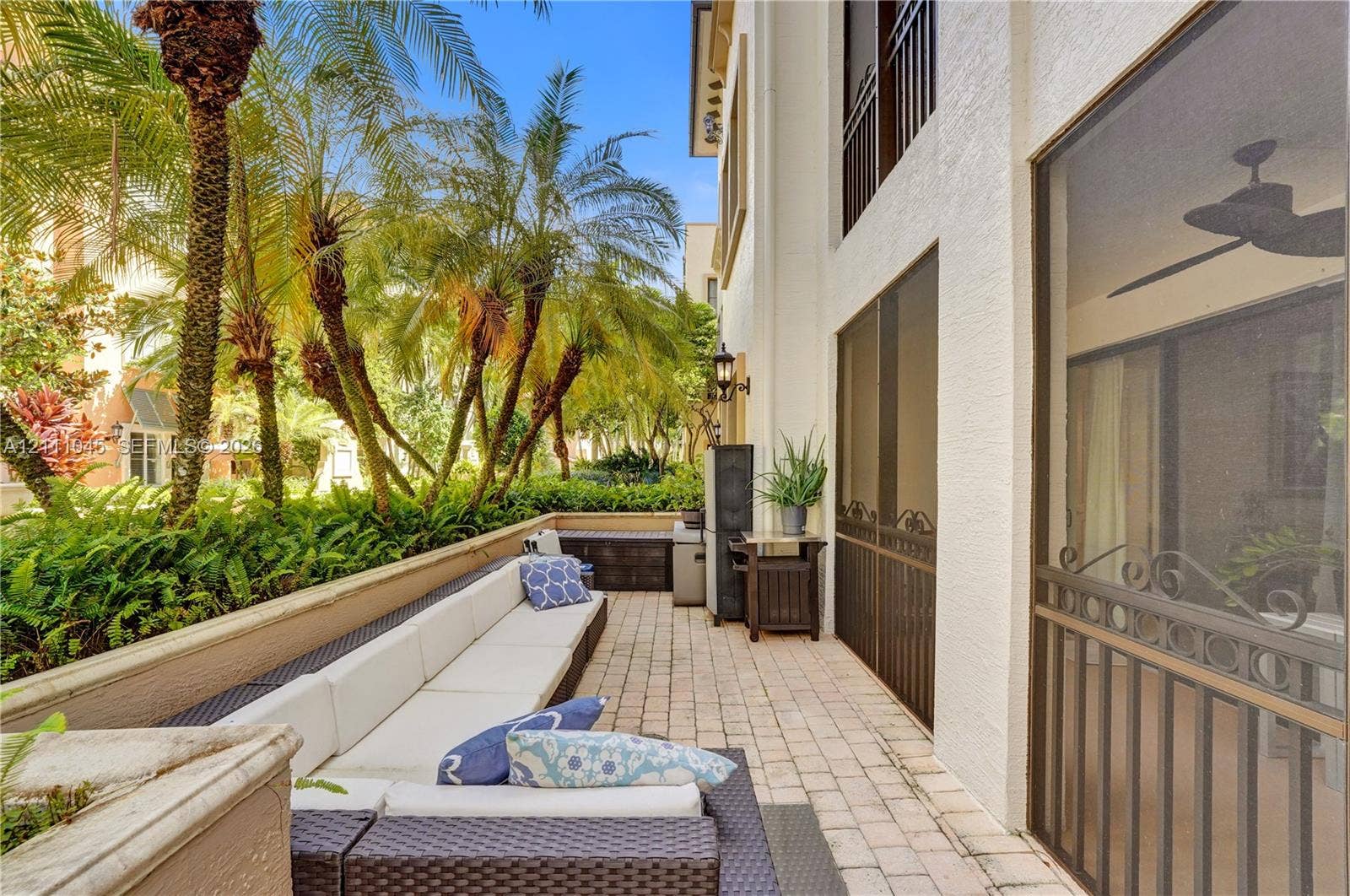 2901 NW 126th Avenue, #2-225, Sunrise, FL 33323 Covered patio featuring paver flooring, a ceiling fan, screen enclosures, and a low concrete retaining wall surrounded by mature landscaping