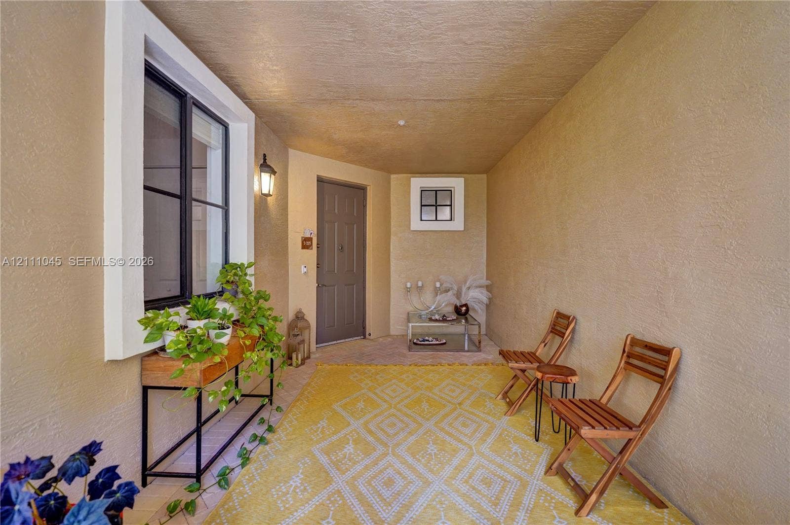 2901 NW 126th Avenue, #2-225, Sunrise, FL 33323 Covered entryway featuring textured stucco walls, a multi-pane window with black framing, a square accent window, and an attached exterior wall-mounted light fixture