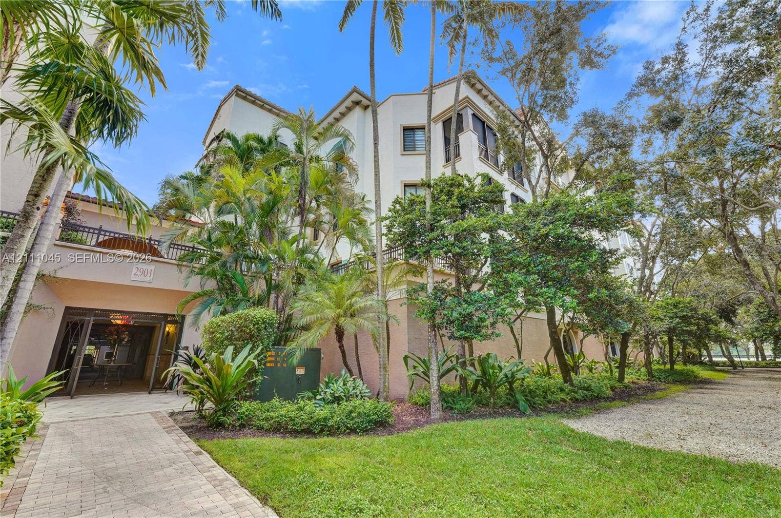 2901 NW 126th Avenue, #2-225, Sunrise, FL 33323 Multi-story exterior featuring light-toned stucco facade, decorative upper-level balconies, paver stone walkway, and established landscaping with mature palm trees