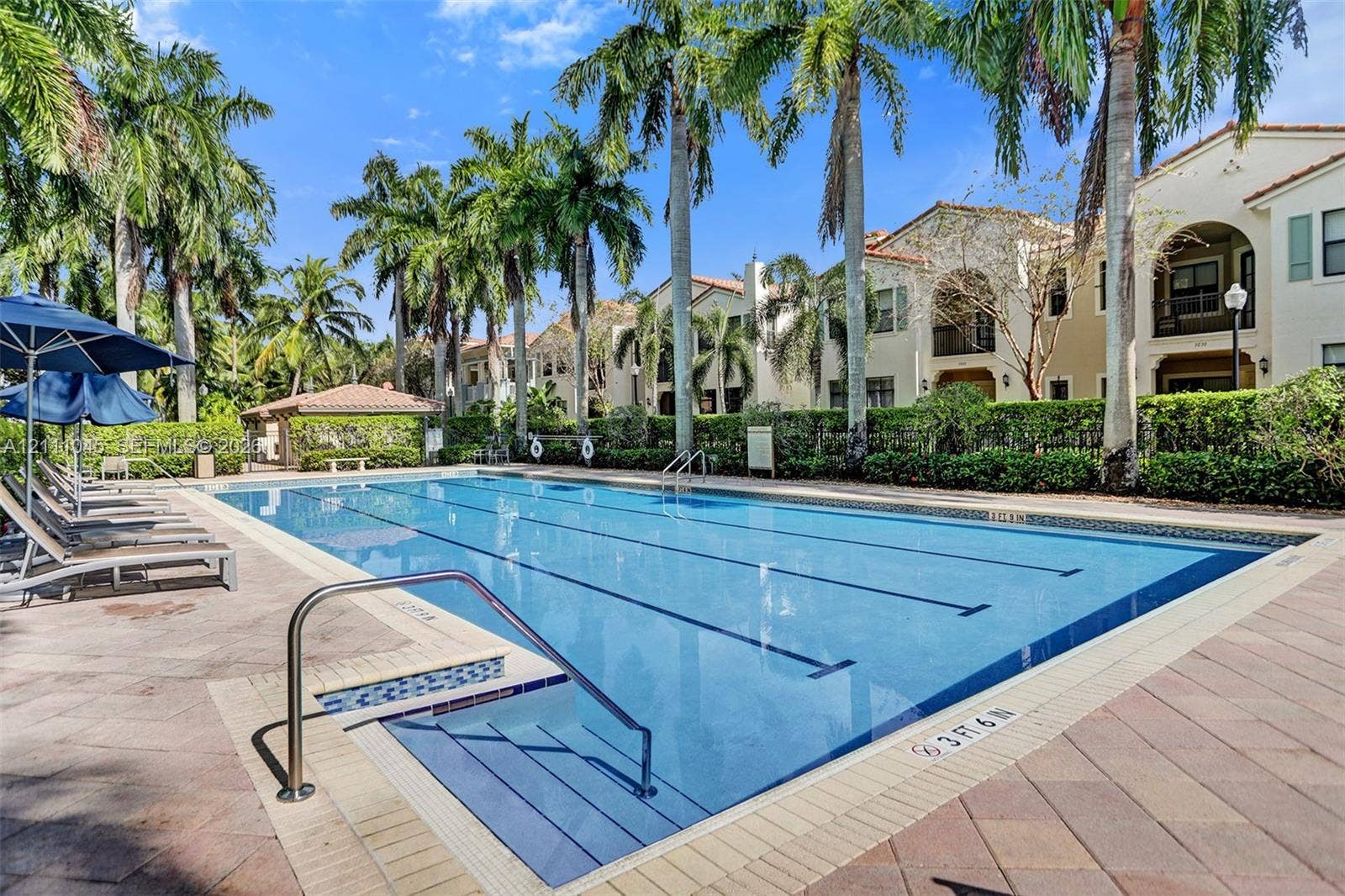 2901 NW 126th Avenue, #2-225, Sunrise, FL 33323 Community lap pool featuring a tiled deck, built-in entry steps with metal handrails, and surrounding mature palm trees