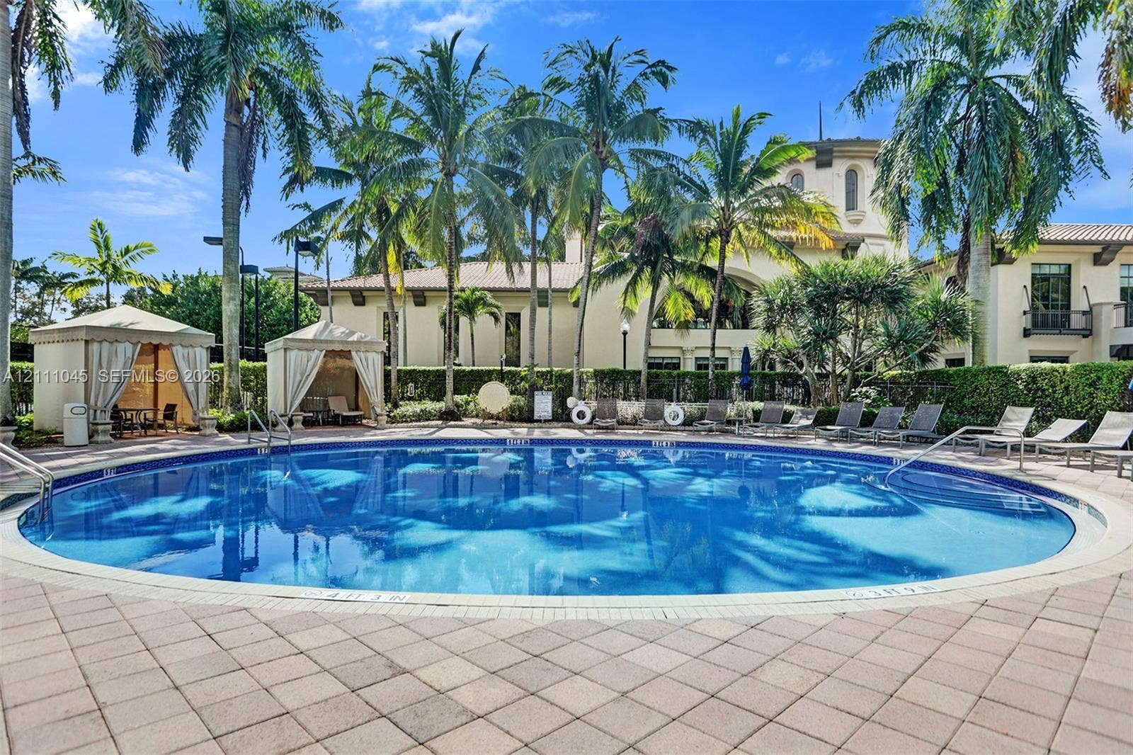 2901 NW 126th Avenue, #2-225, Sunrise, FL 33323 Circular swimming pool featuring a paved stone deck, dual shaded cabanas, and manicured palm tree landscaping