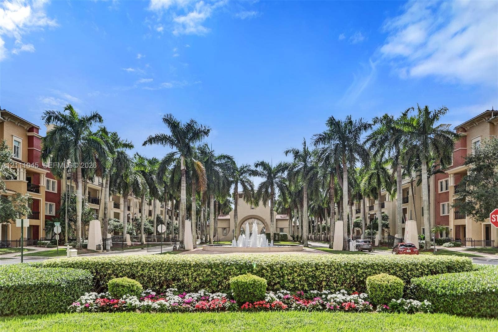 2901 NW 126th Avenue, #2-225, Sunrise, FL 33323 Multi-story residential complex featuring palm-lined drives, manicured hedges, colorful floral beds, and a central tiered water fountain
