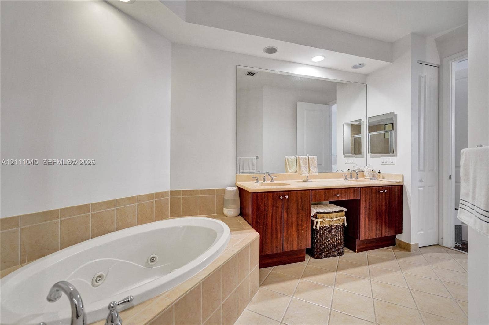2901 NW 126th Avenue, #2-225, Sunrise, FL 33323 Double vanity with wood-finish cabinetry, solid surface countertop, soaking tub with tile surround, and full-width wall mirror