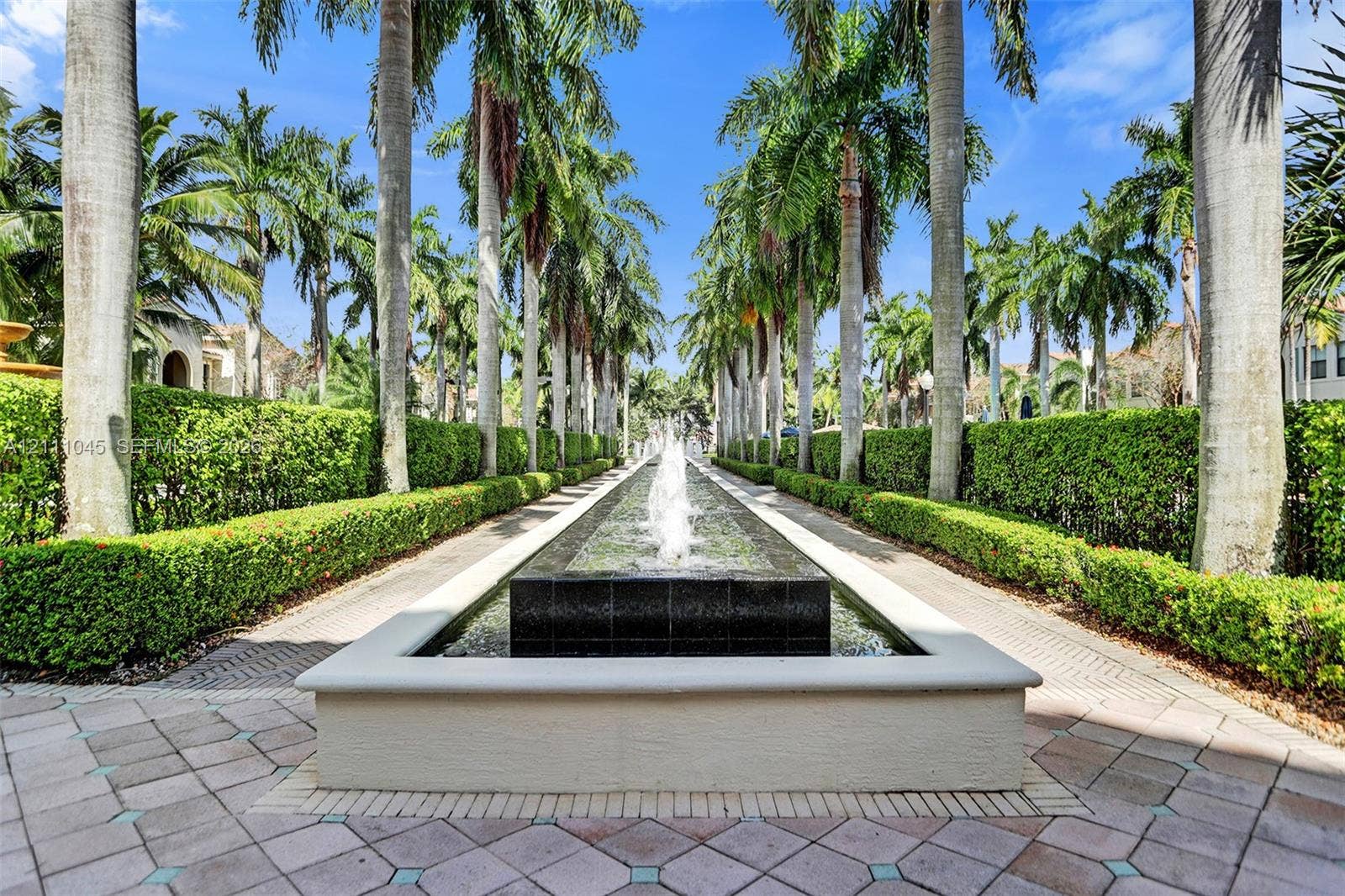 2901 NW 126th Avenue, #2-225, Sunrise, FL 33323 Linear water feature with a central fountain, bordered by manicured hedges, towering palm trees, and decorative paver hardscaping