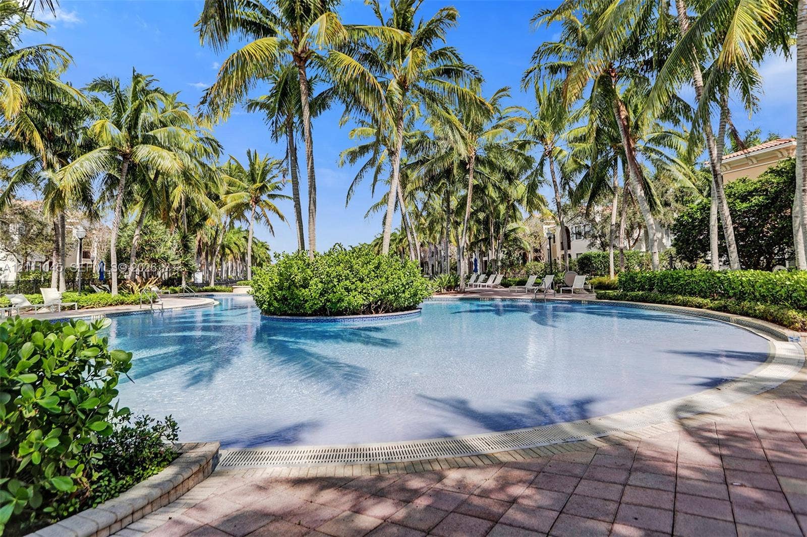 2901 NW 126th Avenue, #2-225, Sunrise, FL 33323 Curved swimming pool featuring a central island landscape, stone-paver decking, and mature palm tree canopy