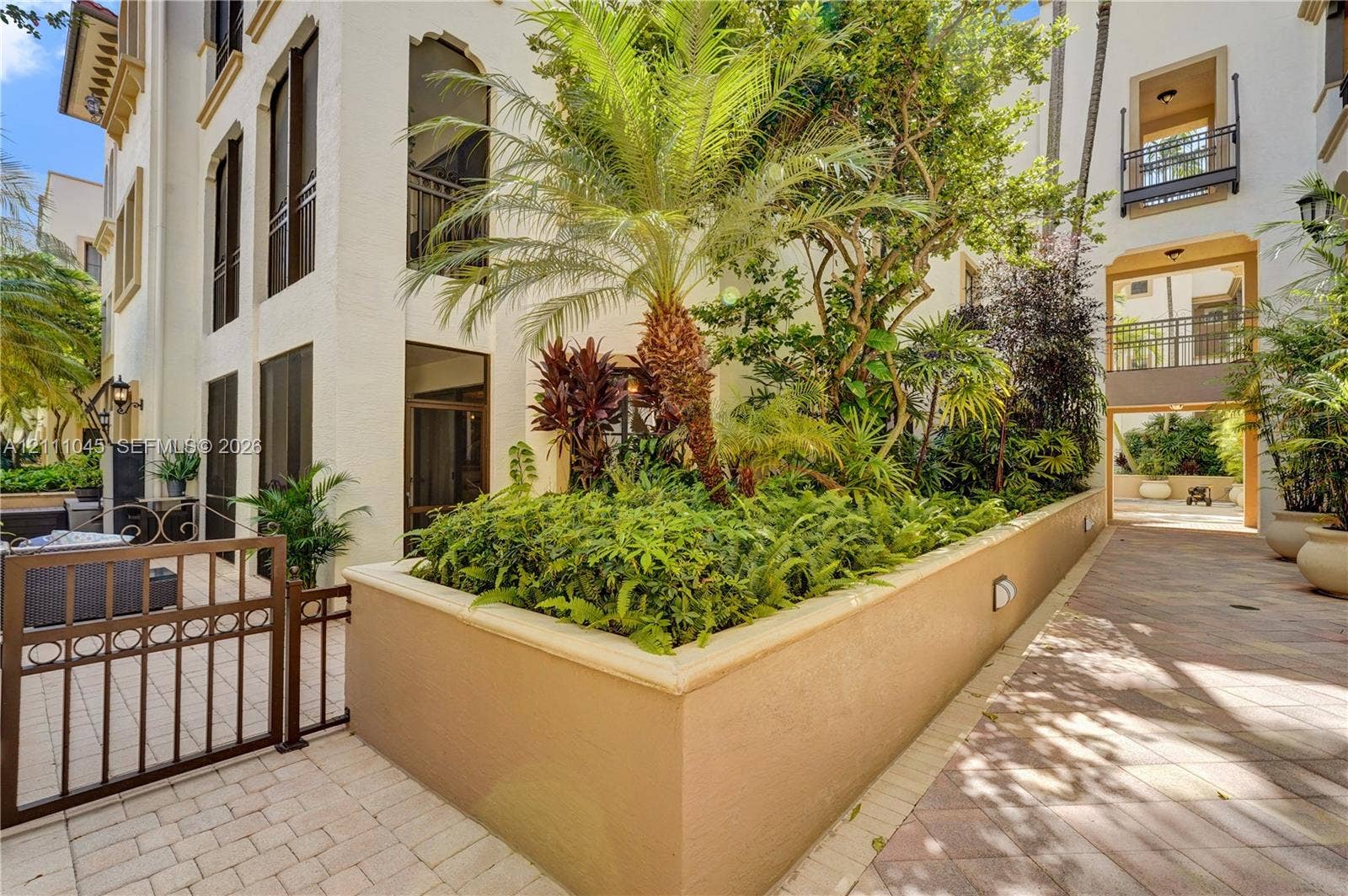 2901 NW 126th Avenue, #2-225, Sunrise, FL 33323 Mediterranean-style exterior featuring a stucco facade, raised masonry garden bed, integrated wrought-iron gate, stone-paver hardscaping, and multi-level balconies with decorative railings