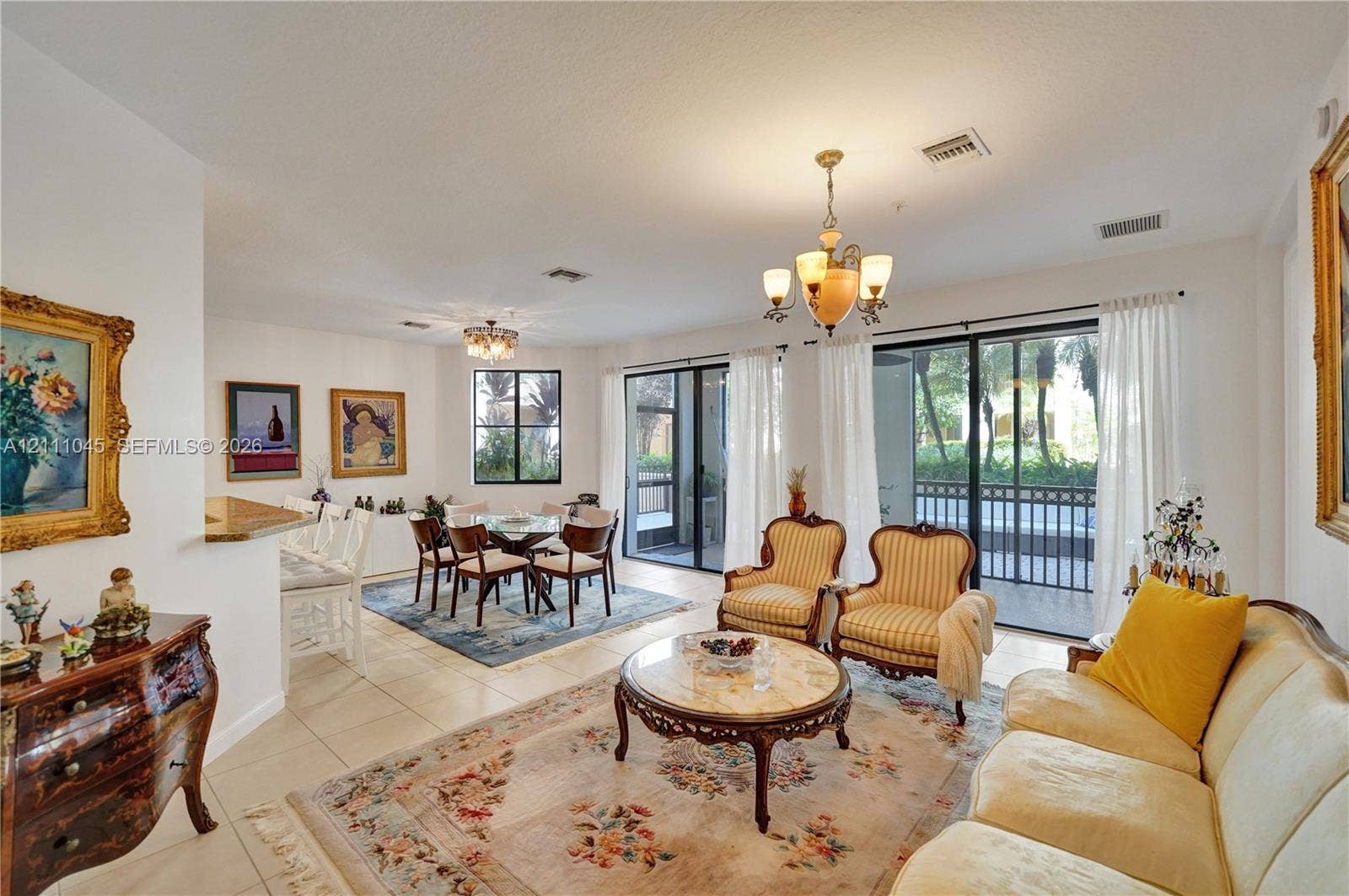 2901 NW 126th Avenue, #2-225, Sunrise, FL 33323 Open-concept living space featuring large-format tile flooring, dual multi-light chandeliers, built-in breakfast bar with stone-finish countertop, and floor-to-ceiling sliding glass doors leading to a screened exterior area