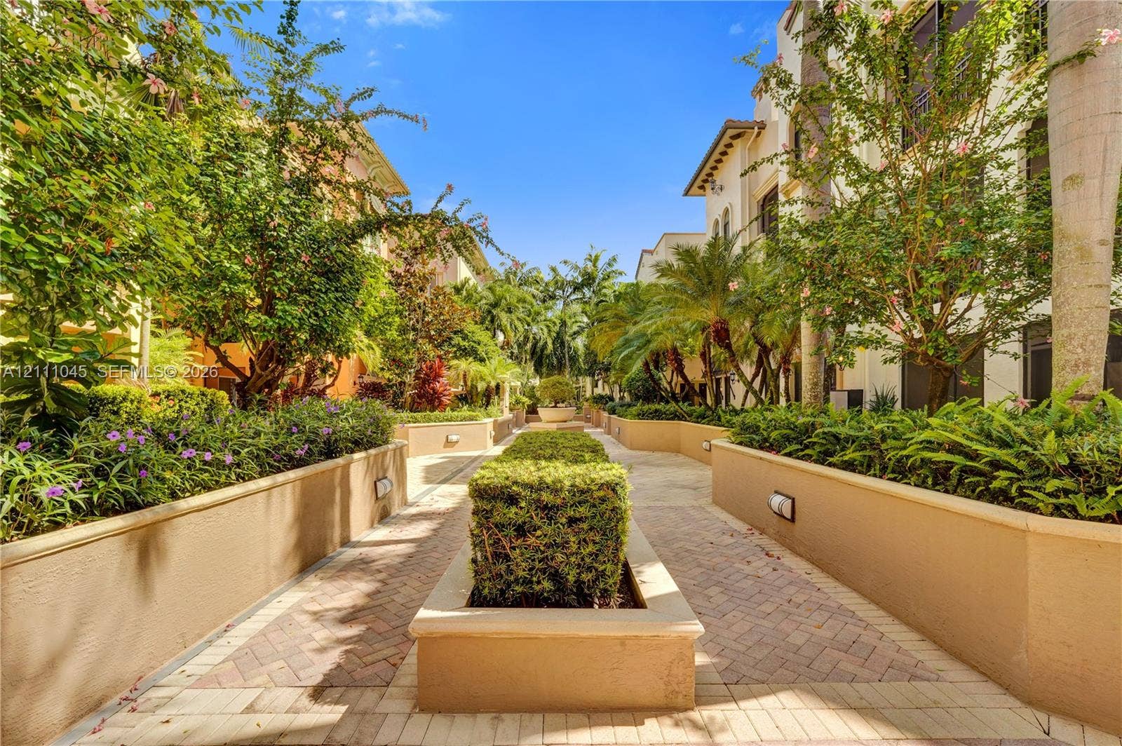 2901 NW 126th Avenue, #2-225, Sunrise, FL 33323 Paver walkway lined with stucco planters, manicured hedges, mature palm trees, and integrated wall lighting