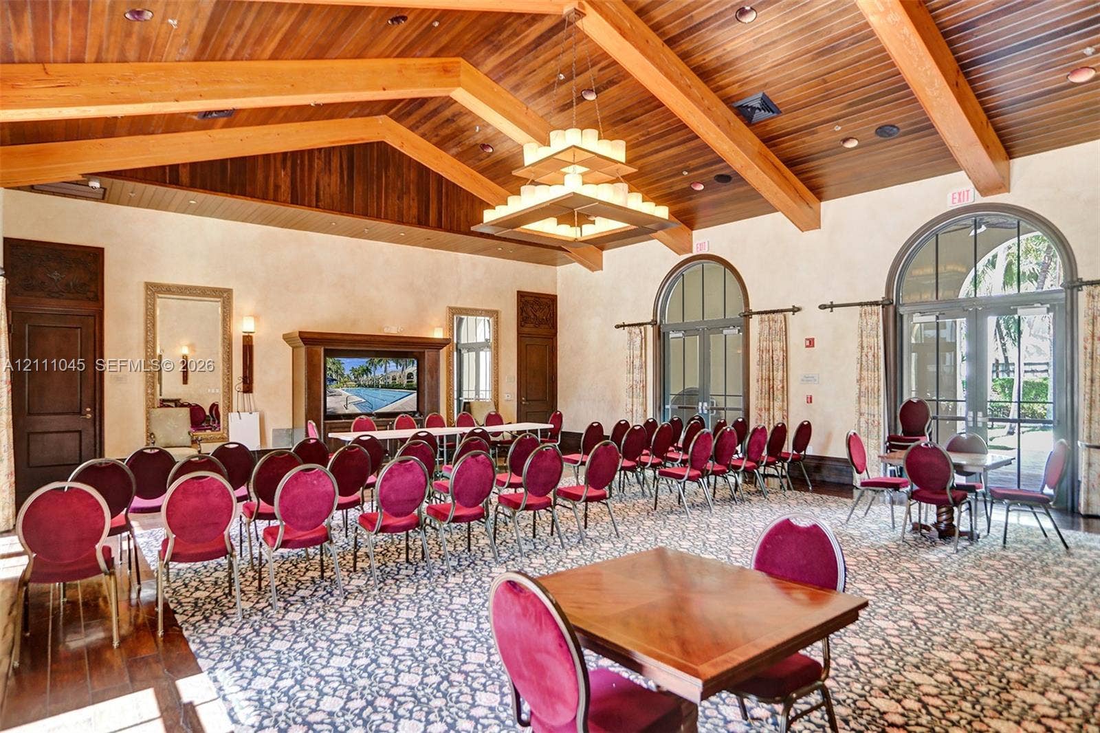 2901 NW 126th Avenue, #2-225, Sunrise, FL 33323 Vaulted wood-plank ceiling with exposed timber beams, tiered chandelier, built-in media cabinetry, and arched glass-paneled doors