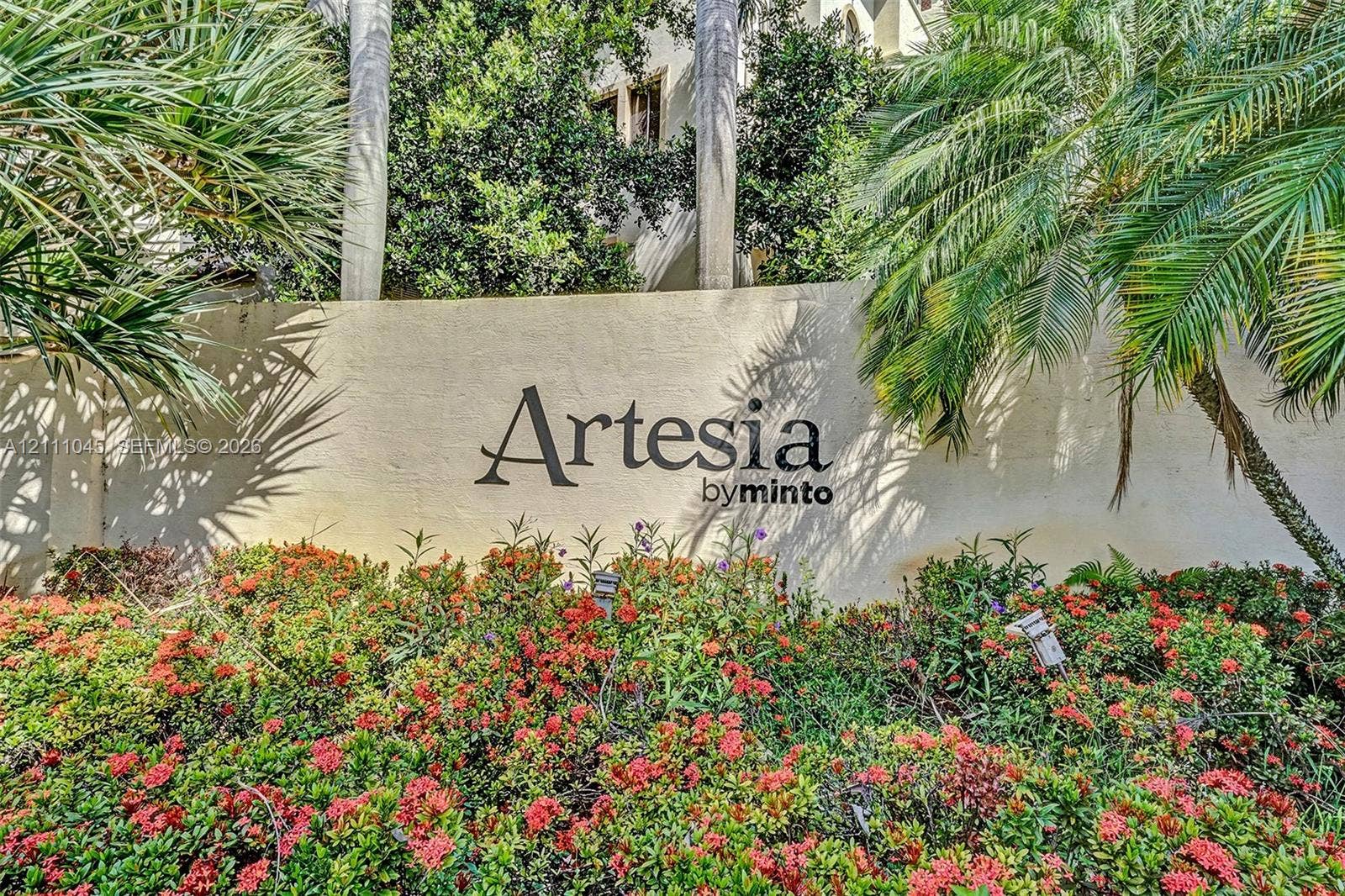 2901 NW 126th Avenue, #2-225, Sunrise, FL 33323 Community monument signage featuring dimensional lettering set against a smooth stucco wall, surrounded by mature palm trees and established flowering shrubbery