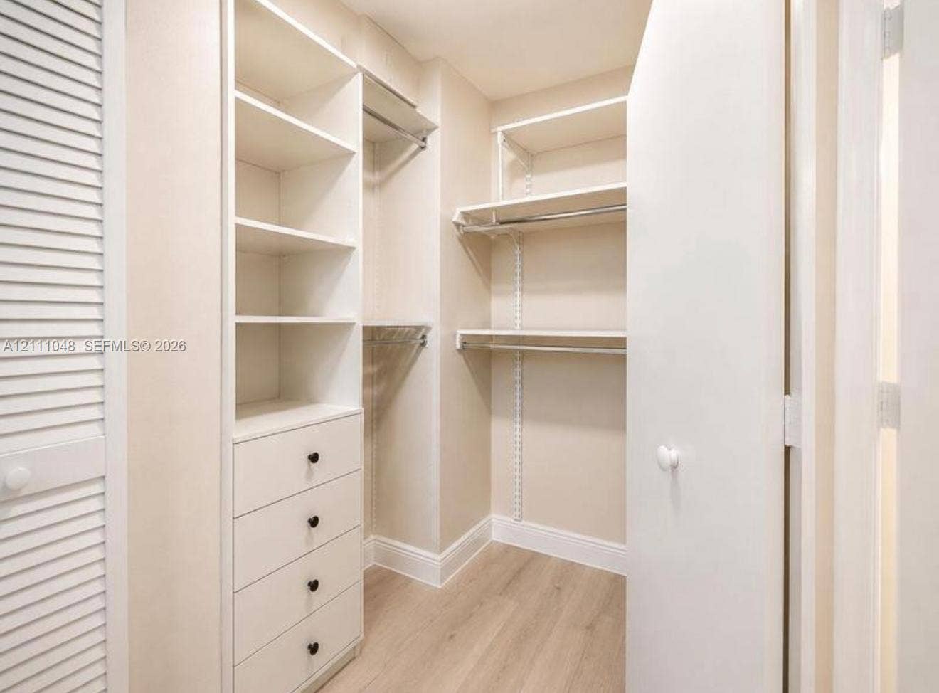 2775 NE 187th Street, #408, Aventura, Aventura, FL 33180 Walk-in closet featuring custom built-in shelving, integrated four-drawer storage, polished metal hanging rods, wood-finish flooring, and a white louvered door