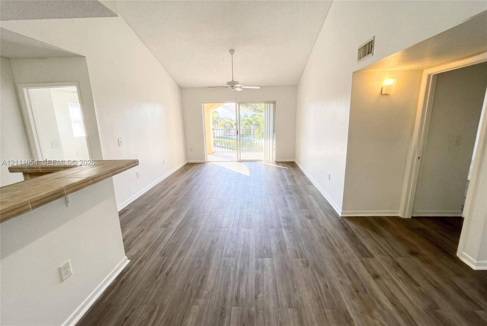 4180 San Marino Boulevard, #106, West Palm Beach, FL 33409 Living area featuring vaulted ceilings, wood-finish flooring, a ceiling fan, a tiled breakfast bar, and sliding glass doors