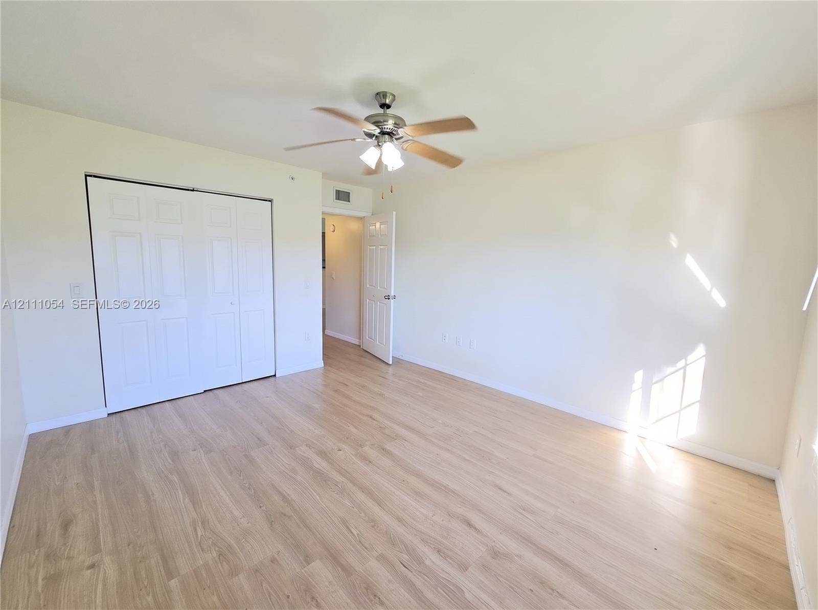 4180 San Marino Boulevard, #106, West Palm Beach, FL 33409 Room featuring wood-finish flooring, a ceiling fan with integrated lighting, and a six-panel sliding closet door