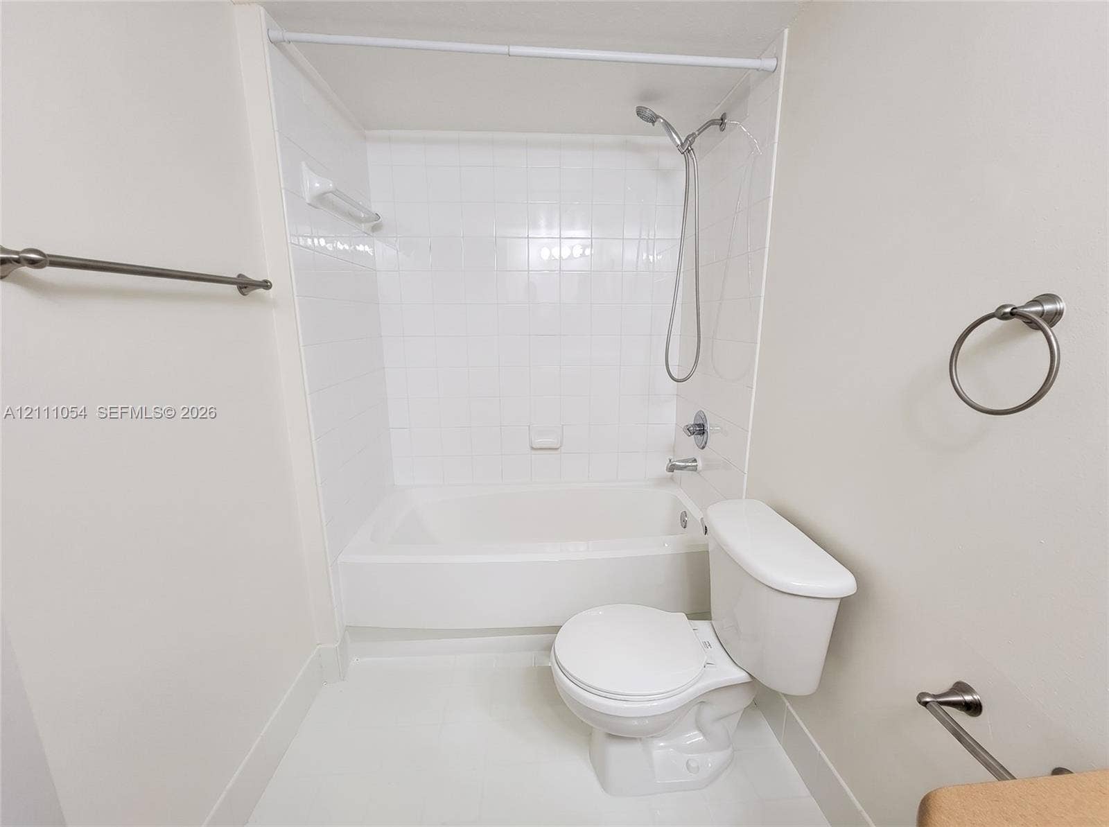 4180 San Marino Boulevard, #106, West Palm Beach, FL 33409 Bathroom featuring a tub-shower combination with white ceramic tile surround, a handheld showerhead, a two-piece toilet, and polished metal hardware