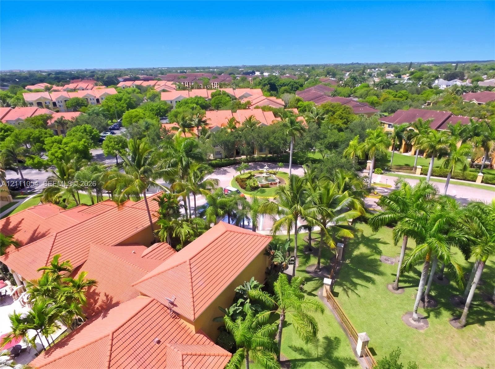 4180 San Marino Boulevard, #106, West Palm Beach, FL 33409 Aerial perspective of terracotta-tiled rooflines, expansive manicured grounds, mature palm trees, and a decorative central fountain