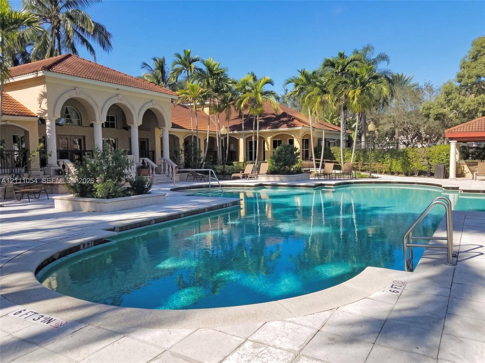 4180 San Marino Boulevard, #106, West Palm Beach, FL 33409 In-ground swimming pool featuring a tiled deck, metal handrails, and arched masonry architecture