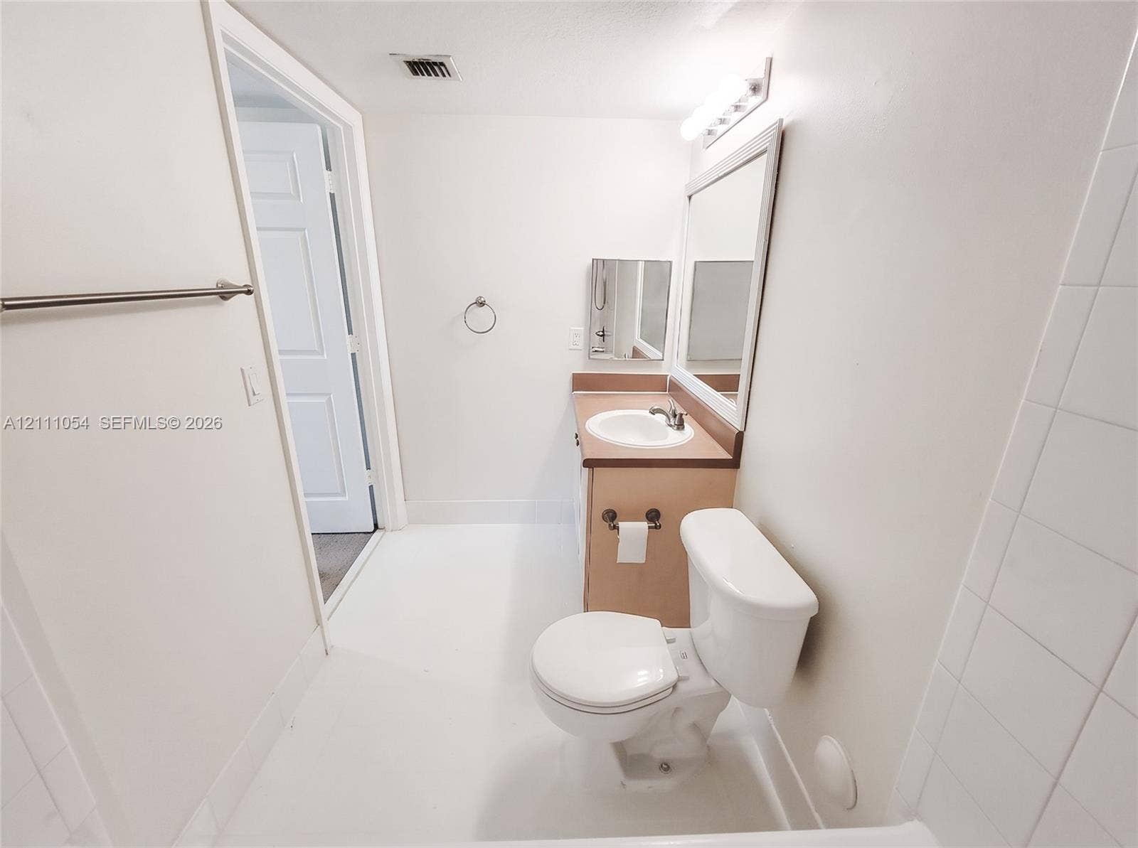 4180 San Marino Boulevard, #106, West Palm Beach, FL 33409 Bathroom featuring a vanity with integrated sink, rectangular wall-mounted mirror, overhead vanity lighting, and wall-mounted towel bar