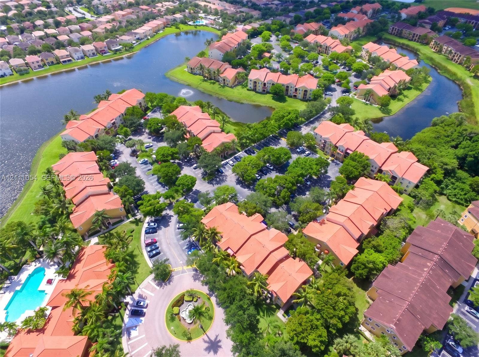 4180 San Marino Boulevard, #106, West Palm Beach, FL 33409 Aerial perspective of a multi-unit complex featuring terra-cotta tile roofs, waterfront positioning, an outdoor swimming pool, and mature perimeter landscaping