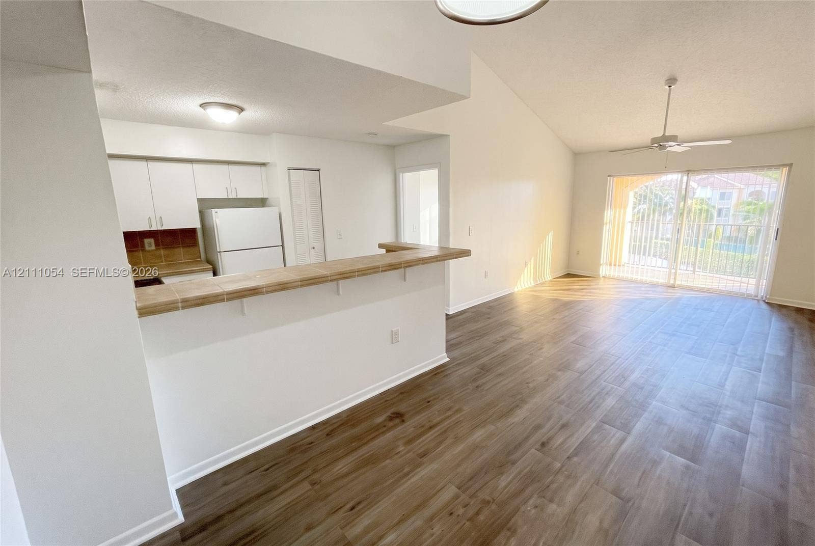 4180 San Marino Boulevard, #106, West Palm Beach, FL 33409 Open-concept kitchen featuring a tile-topped breakfast bar, wood-finish flooring, vaulted ceilings, and glass sliding doors
