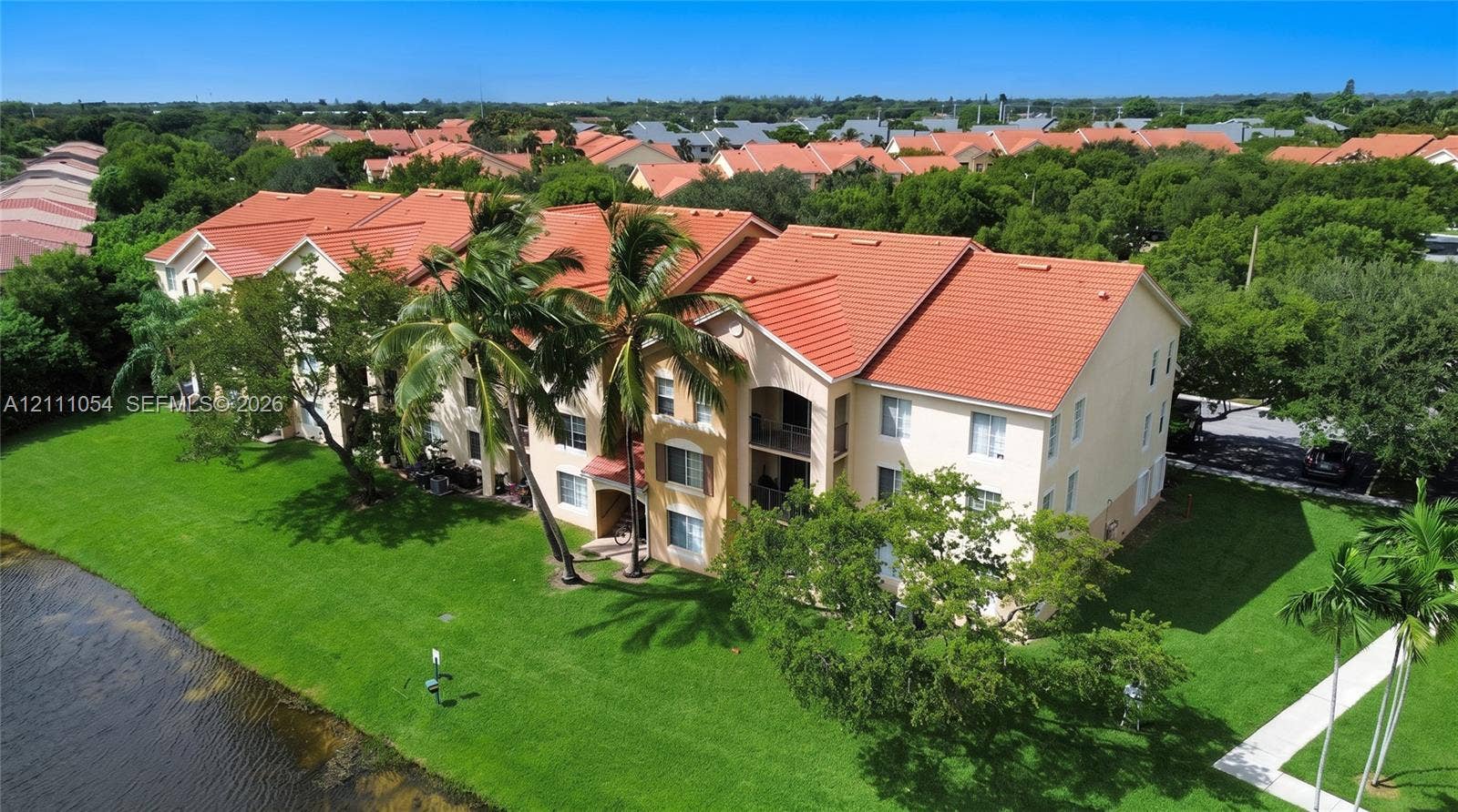 4180 San Marino Boulevard, #106, West Palm Beach, FL 33409 Multi-story building with terracotta-style roof tiles, stucco exterior, private balconies, and waterfront positioning surrounded by mature landscaping