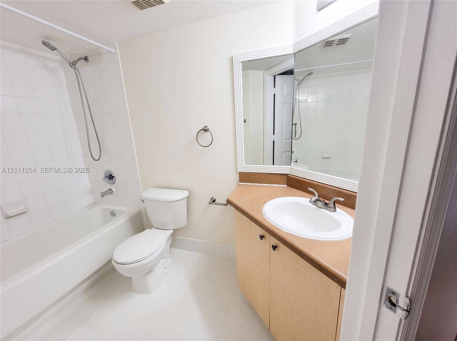 4180 San Marino Boulevard, #106, West Palm Beach, FL 33409 Full bathroom featuring a tub-shower combination with white wall tile, a vanity with a solid-surface countertop and integrated sink, and an expansive corner-mounted vanity mirror
