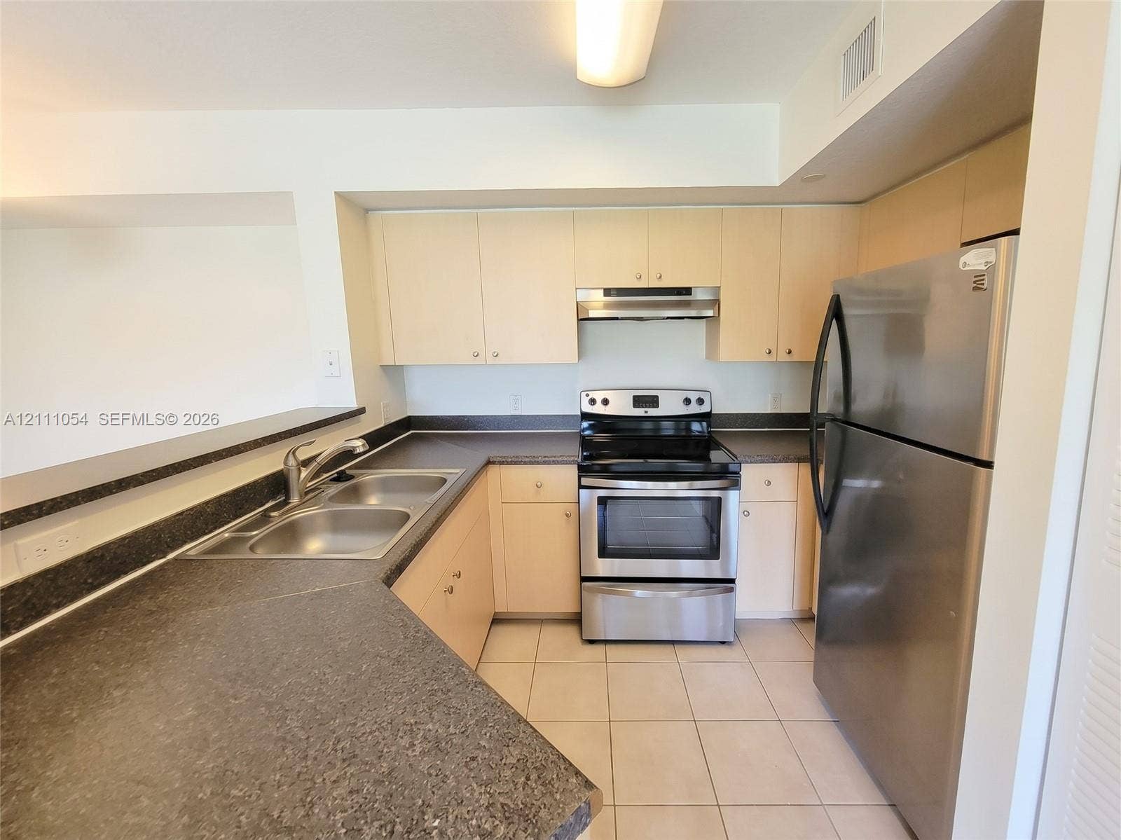 4180 San Marino Boulevard, #106, West Palm Beach, FL 33409 Kitchen featuring light-finish cabinetry, dark solid-surface countertops, stainless steel appliances, double-basin sink, and tile flooring