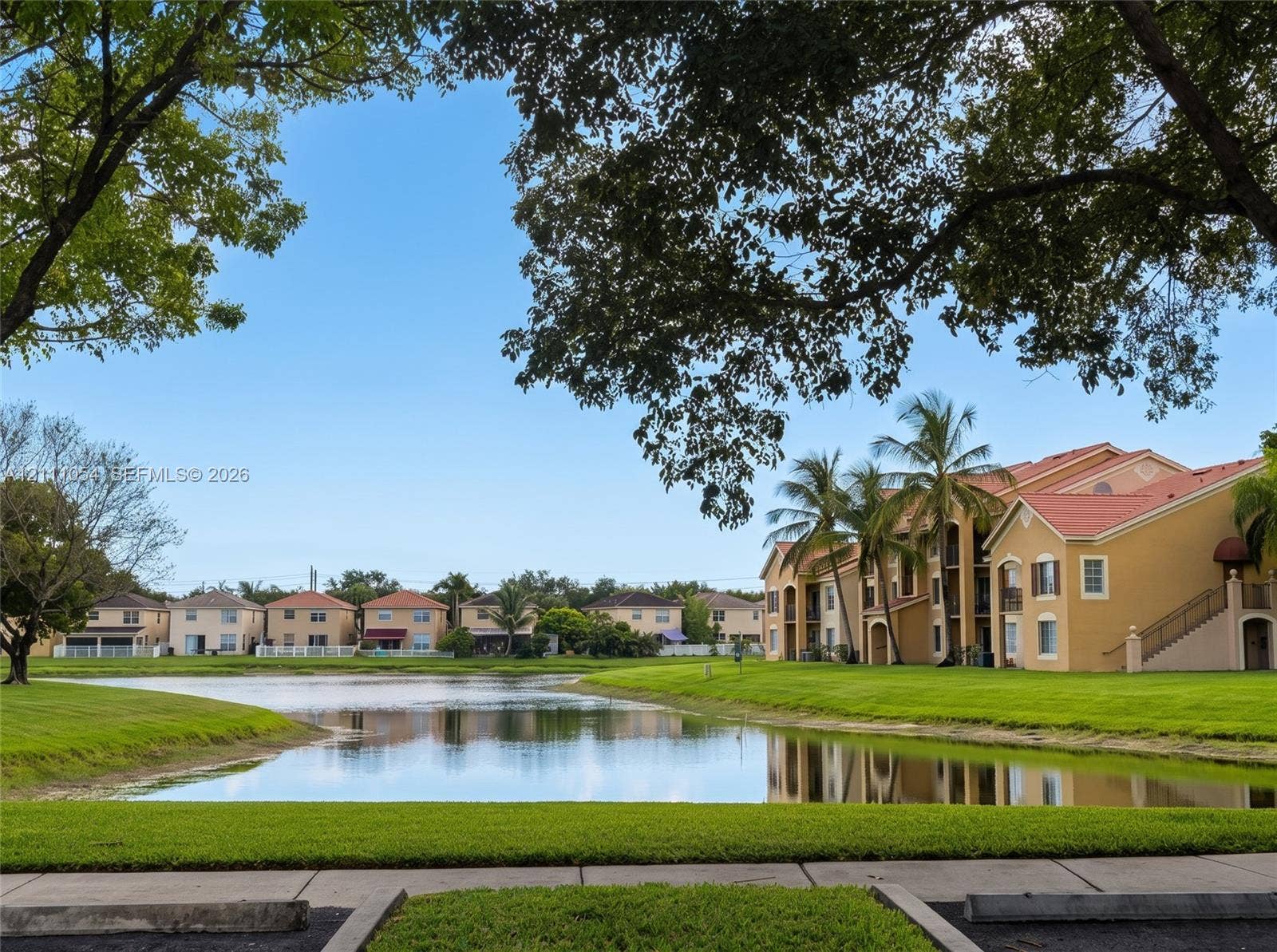 4180 San Marino Boulevard, #106, West Palm Beach, FL 33409 Waterfront setting with manicured lawn, mature trees, and multi-story stucco architecture