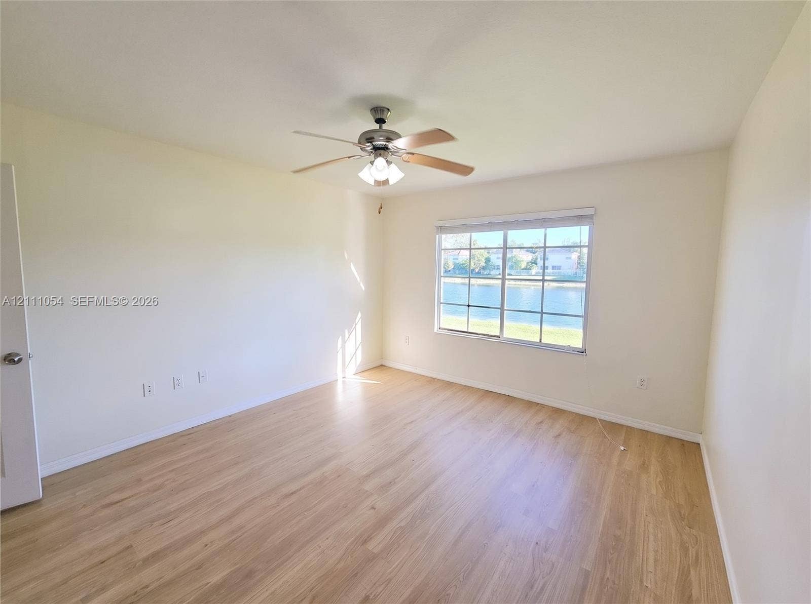 4180 San Marino Boulevard, #106, West Palm Beach, FL 33409 Interior space featuring wood-finish flooring, a ceiling fan with integrated lighting, and a grid-pane window overlooking a water feature