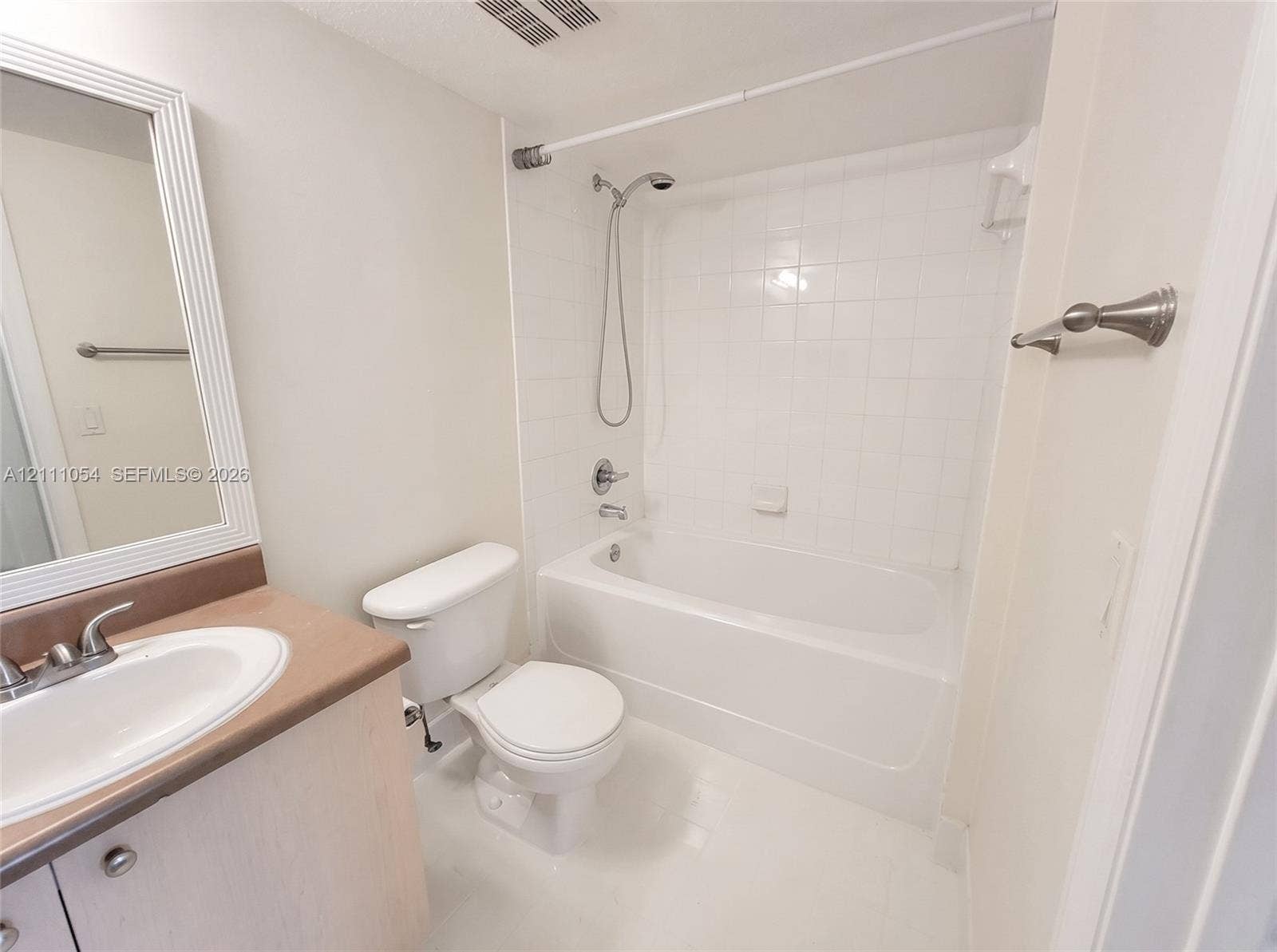 4180 San Marino Boulevard, #106, West Palm Beach, FL 33409 Bathroom featuring a vanity with a solid-surface countertop, an integrated sink with a dual-handle faucet, a white porcelain toilet, and a shower-tub combination with white tile surround and a handheld shower head