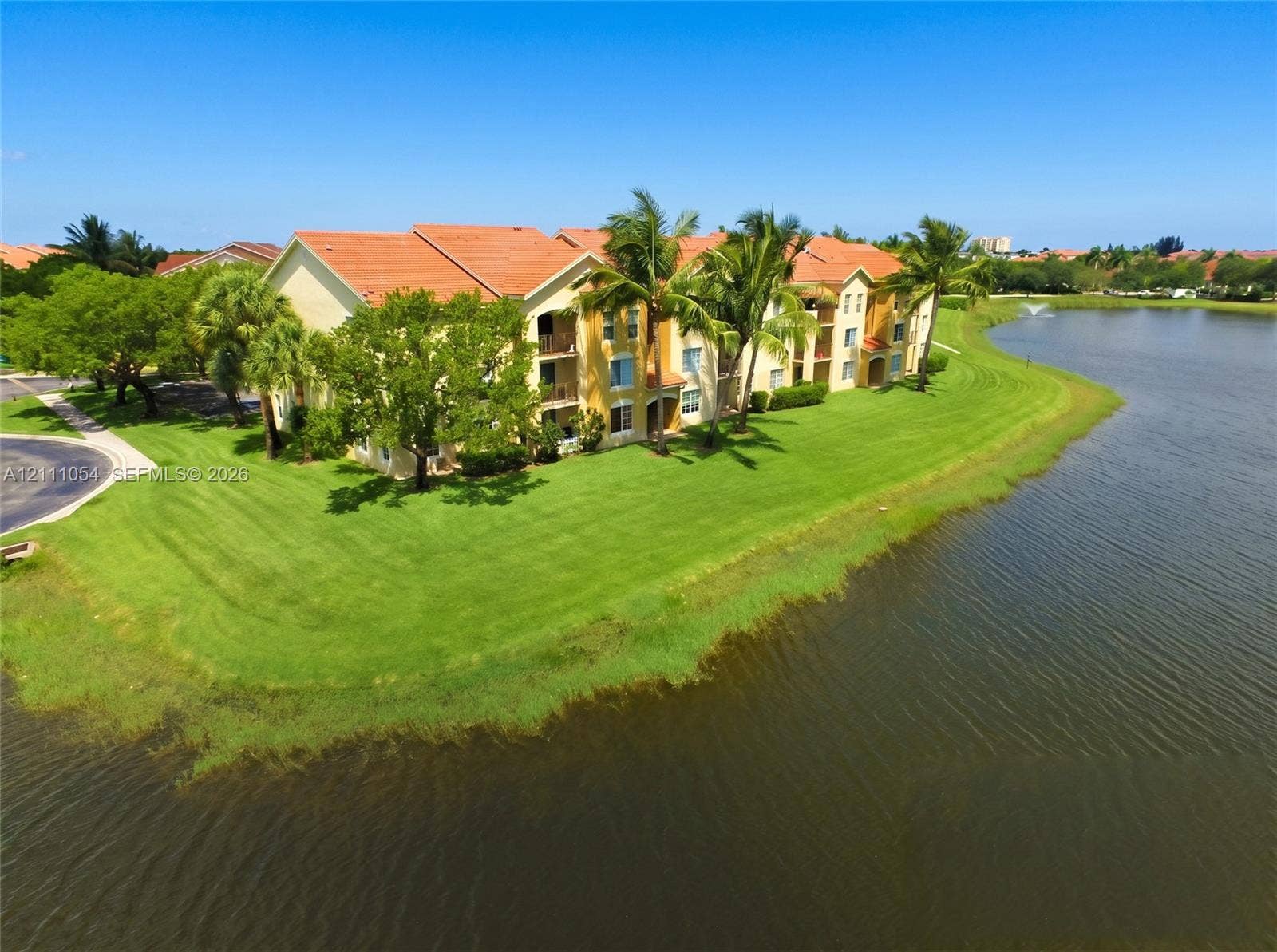 4180 San Marino Boulevard, #106, West Palm Beach, FL 33409 Multi-story residential building featuring a tile roof, stucco exterior, private balconies, and landscaped grounds positioned along a lakefront