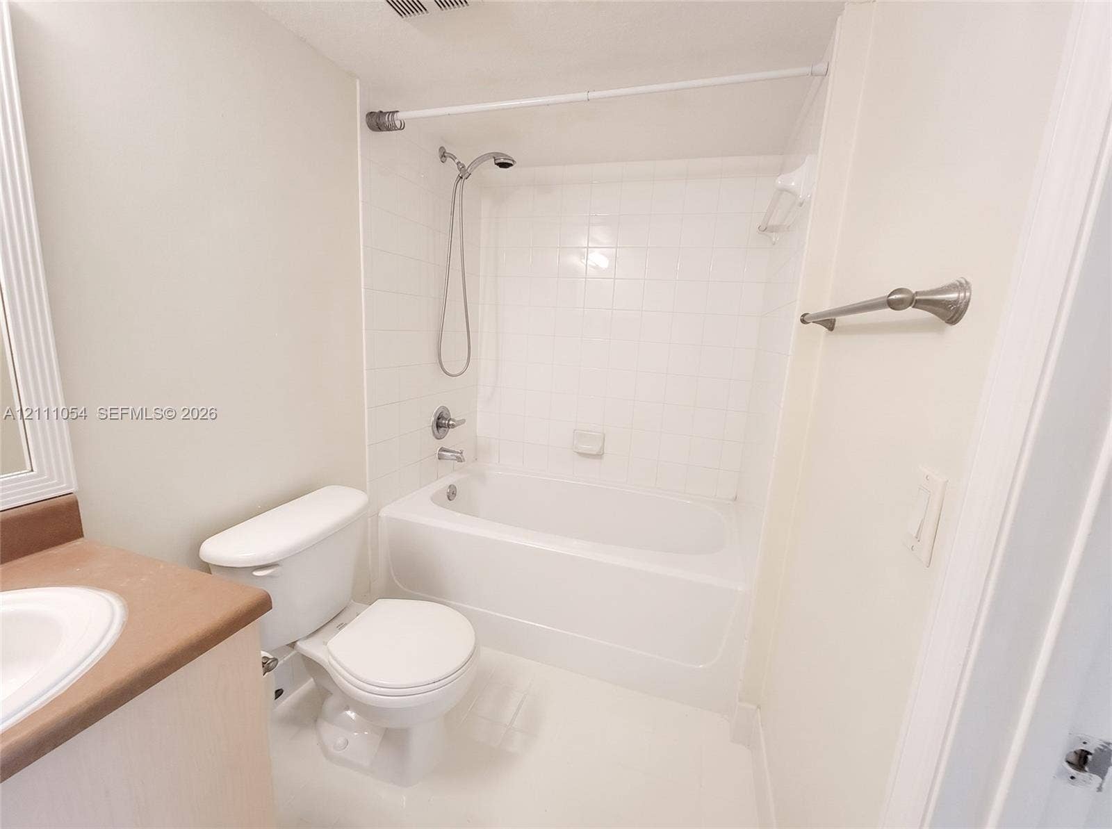 4180 San Marino Boulevard, #106, West Palm Beach, FL 33409 Bathroom featuring a white bathtub with tile surround, handheld shower fixture, vanity with integrated basin, and brushed-finish towel bar