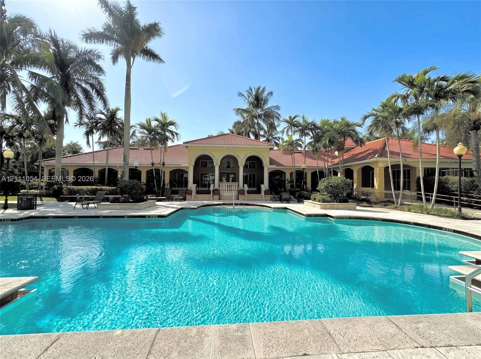 4180 San Marino Boulevard, #106, West Palm Beach, FL 33409 Expansive swimming pool with stone coping, arched architectural detailing, tile roof, and mature palm landscaping