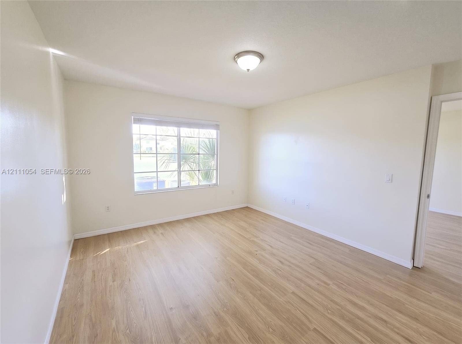 4180 San Marino Boulevard, #106, West Palm Beach, FL 33409 Neutral-toned interior space featuring wood-finish flooring, a grid-pattern window, and a flush-mount ceiling light fixture