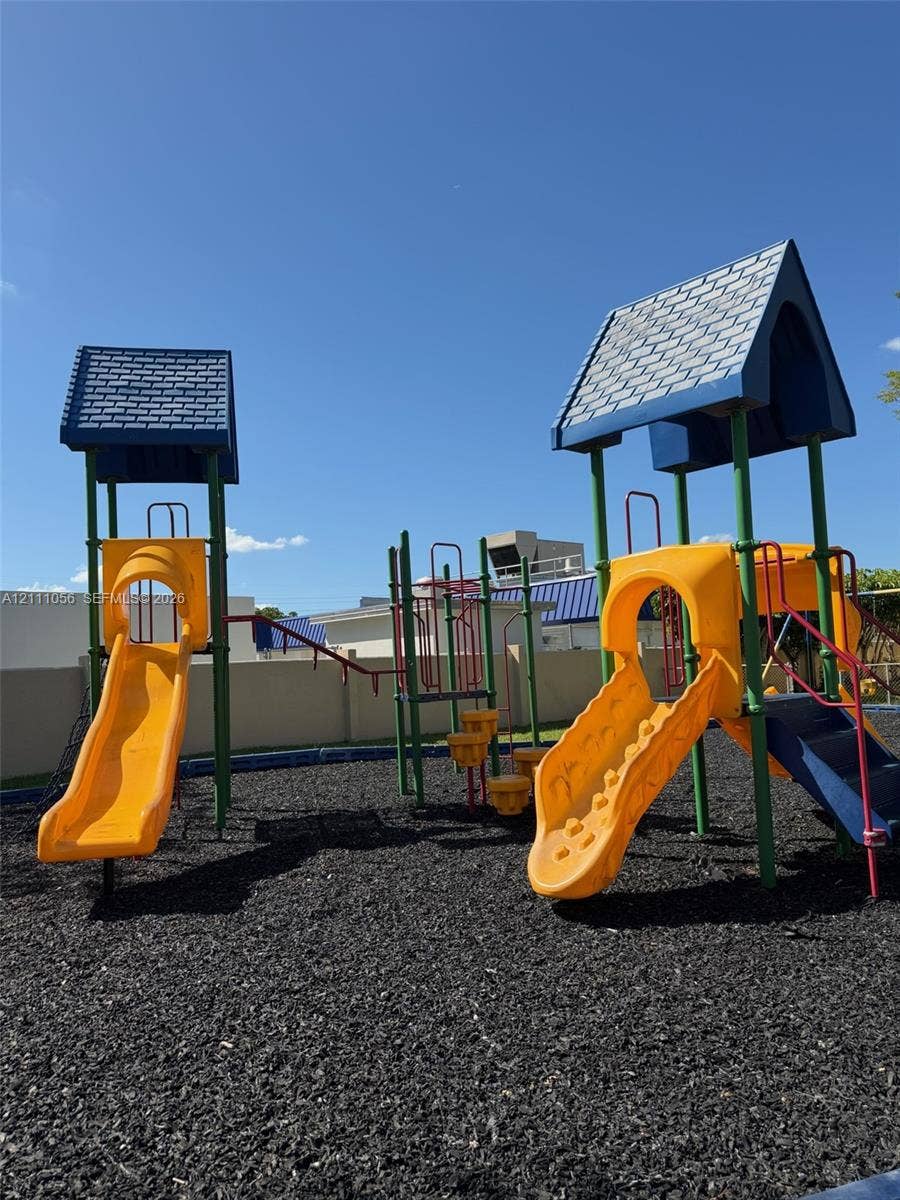 5020 Sheridan Street, #2, Hollywood, FL 33021 Outdoor recreation area featuring two multi-level play structures, molded slides, and ground-level mulch surfacing, enclosed by a perimeter wall