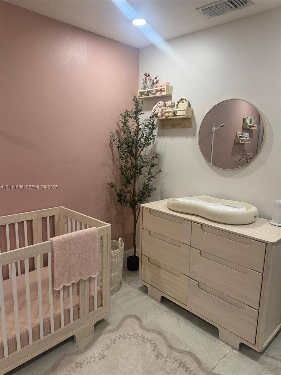 5020 Sheridan Street, #2, Hollywood, FL 33021 Room featuring an accent wall in a muted rose tone, neutral light-finish wood-tone built-in cabinetry, large-format tile flooring, a circular wall-mounted mirror, and recessed lighting