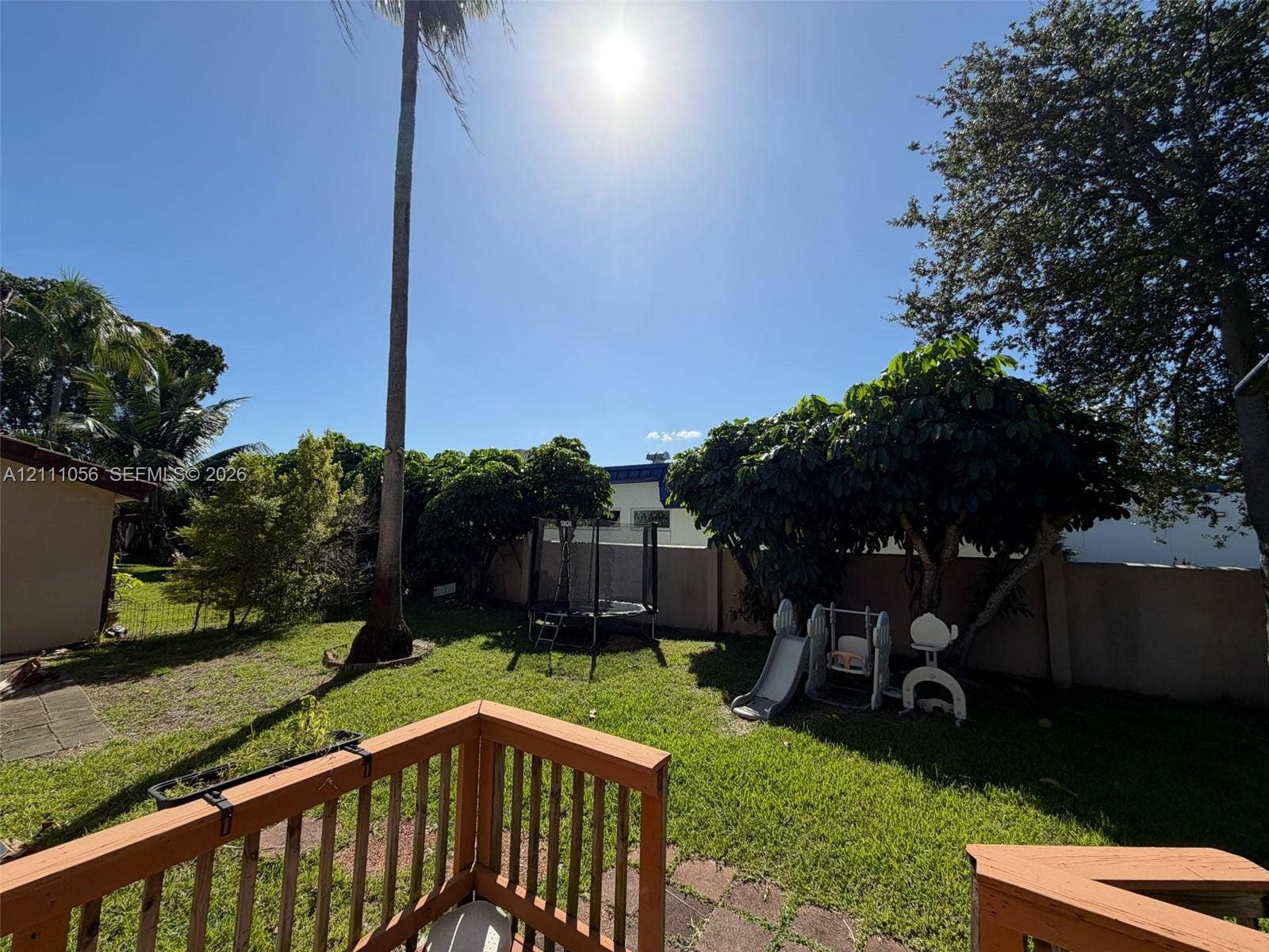 5020 Sheridan Street, #2, Hollywood, FL 33021 Backyard featuring a wood-rail deck, expansive lawn, mature trees, and a solid perimeter wall