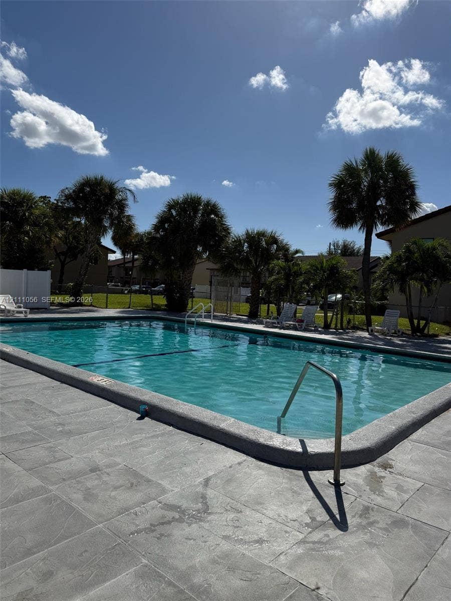 5020 Sheridan Street, #2, Hollywood, FL 33021 In-ground swimming pool featuring a concrete deck, metal handrails, and surrounding palm trees