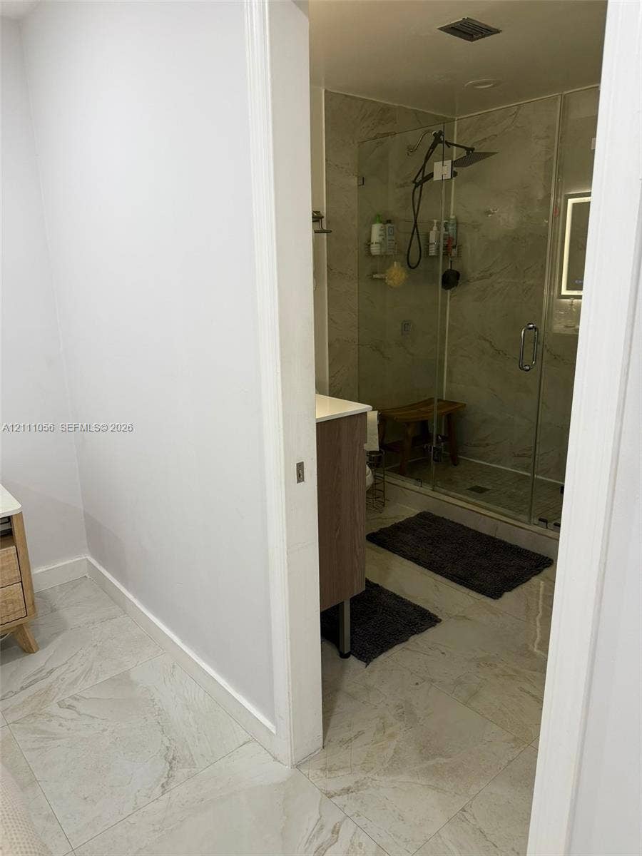 5020 Sheridan Street, #2, Hollywood, FL 33021 Bathroom featuring stone-finish flooring, a wood-finish vanity, and a glass-enclosed shower with a rainfall showerhead