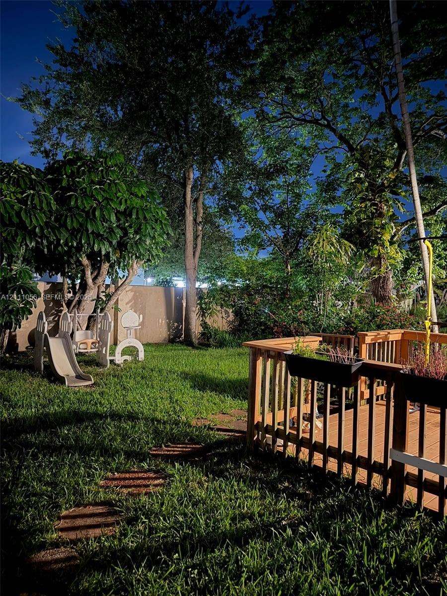 5020 Sheridan Street, #2, Hollywood, FL 33021 Backyard featuring a wood-decked patio with integrated railing, stone paver path, solid perimeter fencing, and mature trees