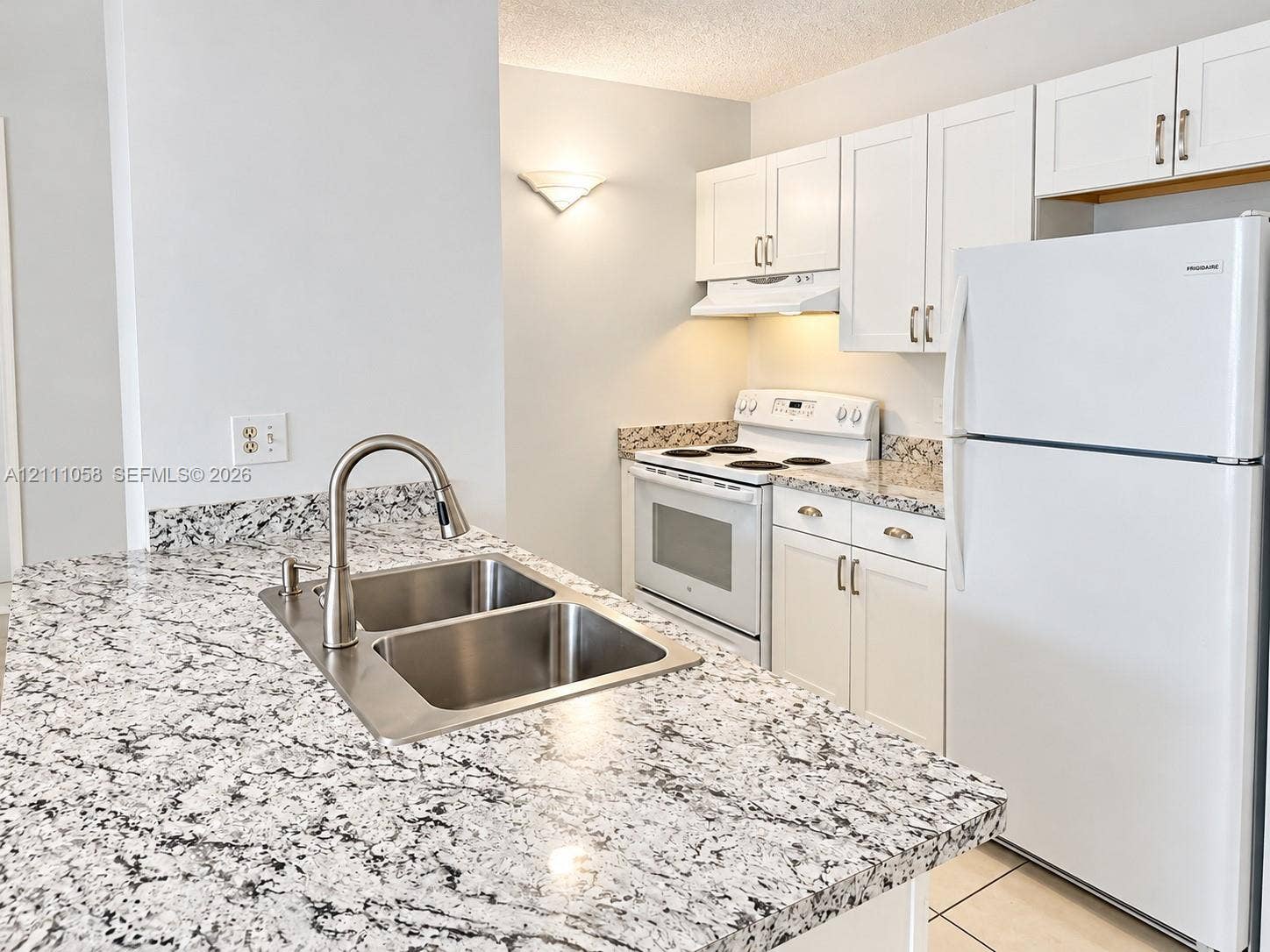 Kitchen featuring speckled stone countertops, dual-basin stainless steel sink with a high-arch faucet, white cabinetry, and matching white appliances