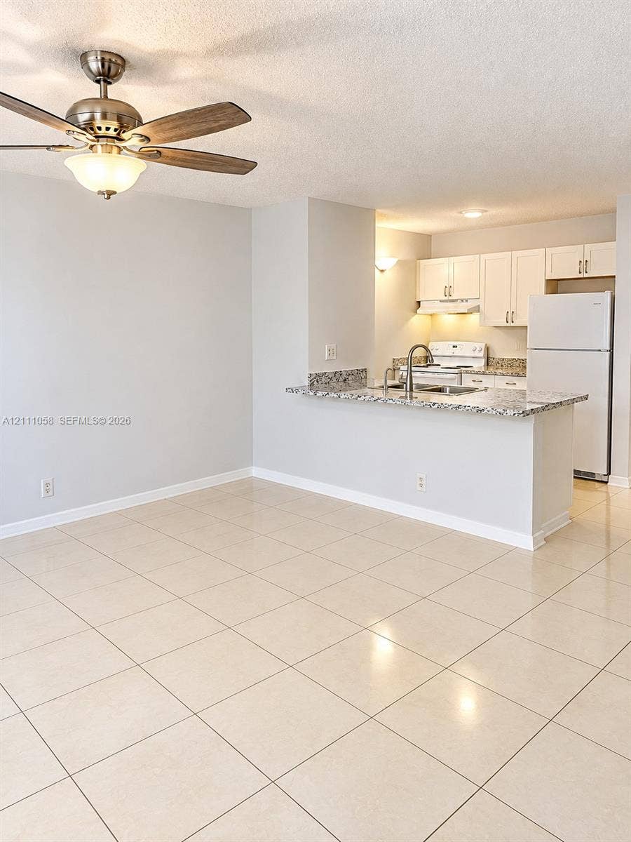 Ceramic tile flooring, breakfast bar with stone-finish countertop, white shaker-style cabinetry, and brushed nickel ceiling fan