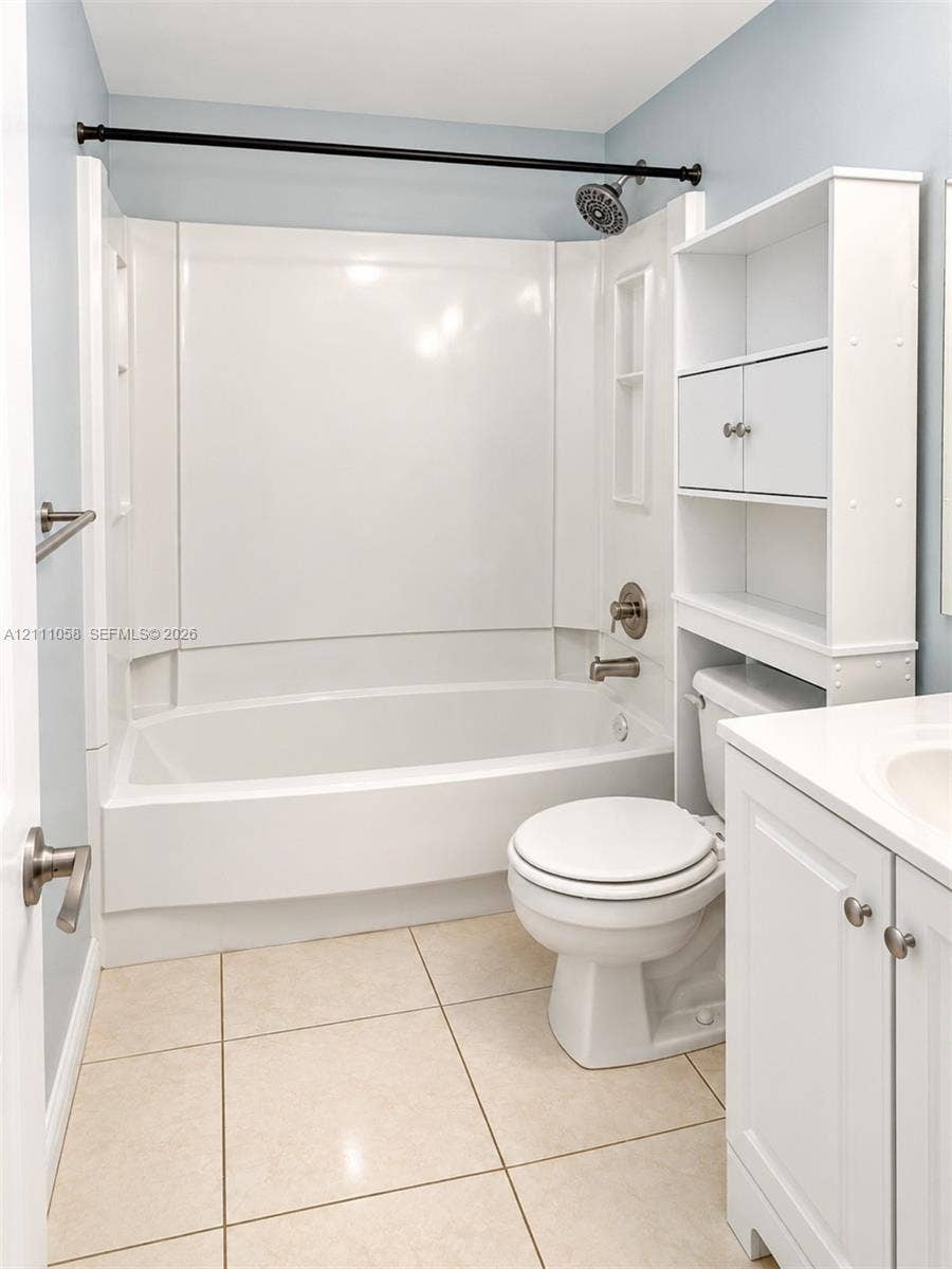 Full-bathroom featuring a tub-shower combination with integrated shelving, white vanity with stone-style countertop, large-format tile flooring, and built-in vertical storage unit